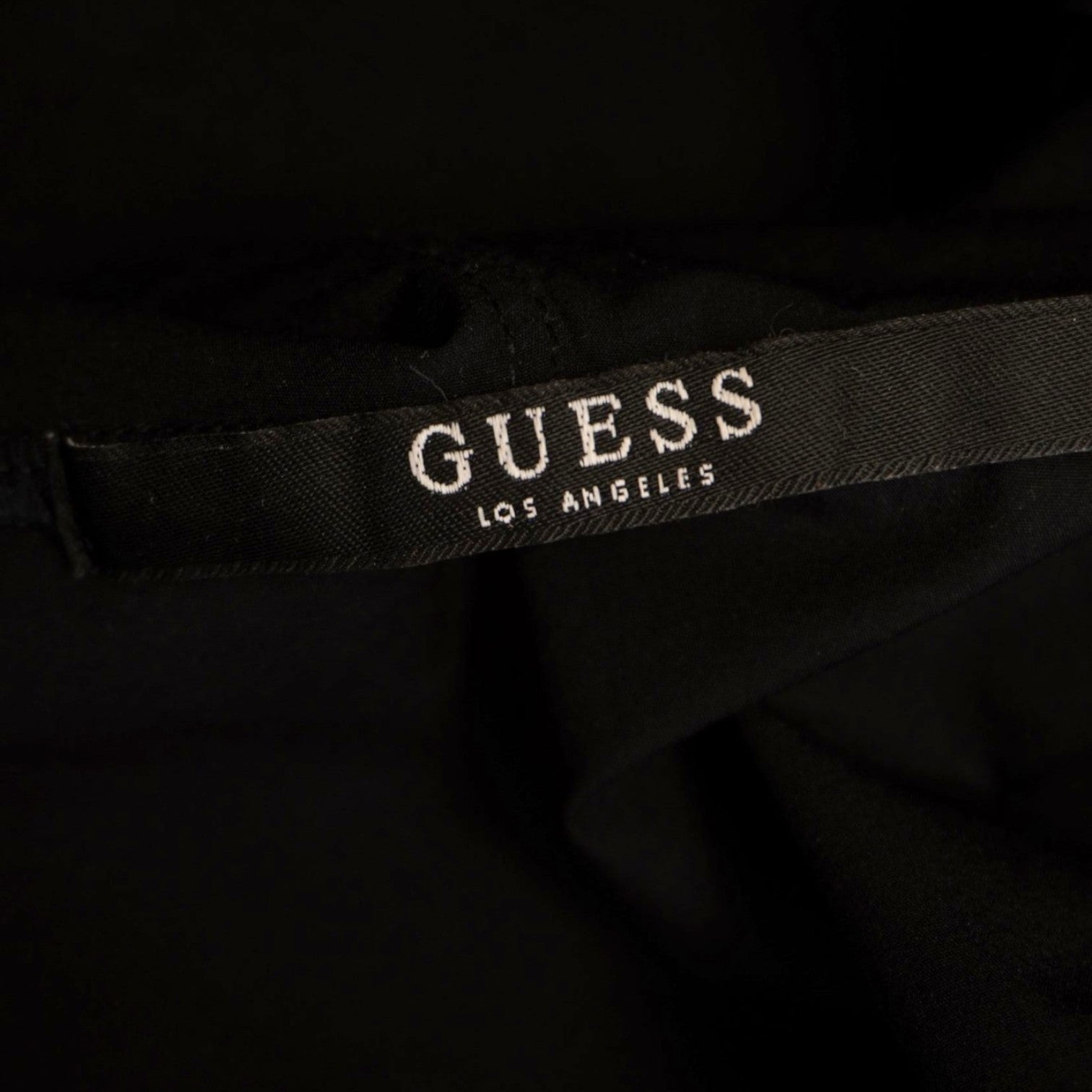 Dettaglio del brand core sul collo interno con la scritta "GUESS Los Angeles" ricamata su fettuccia nera.