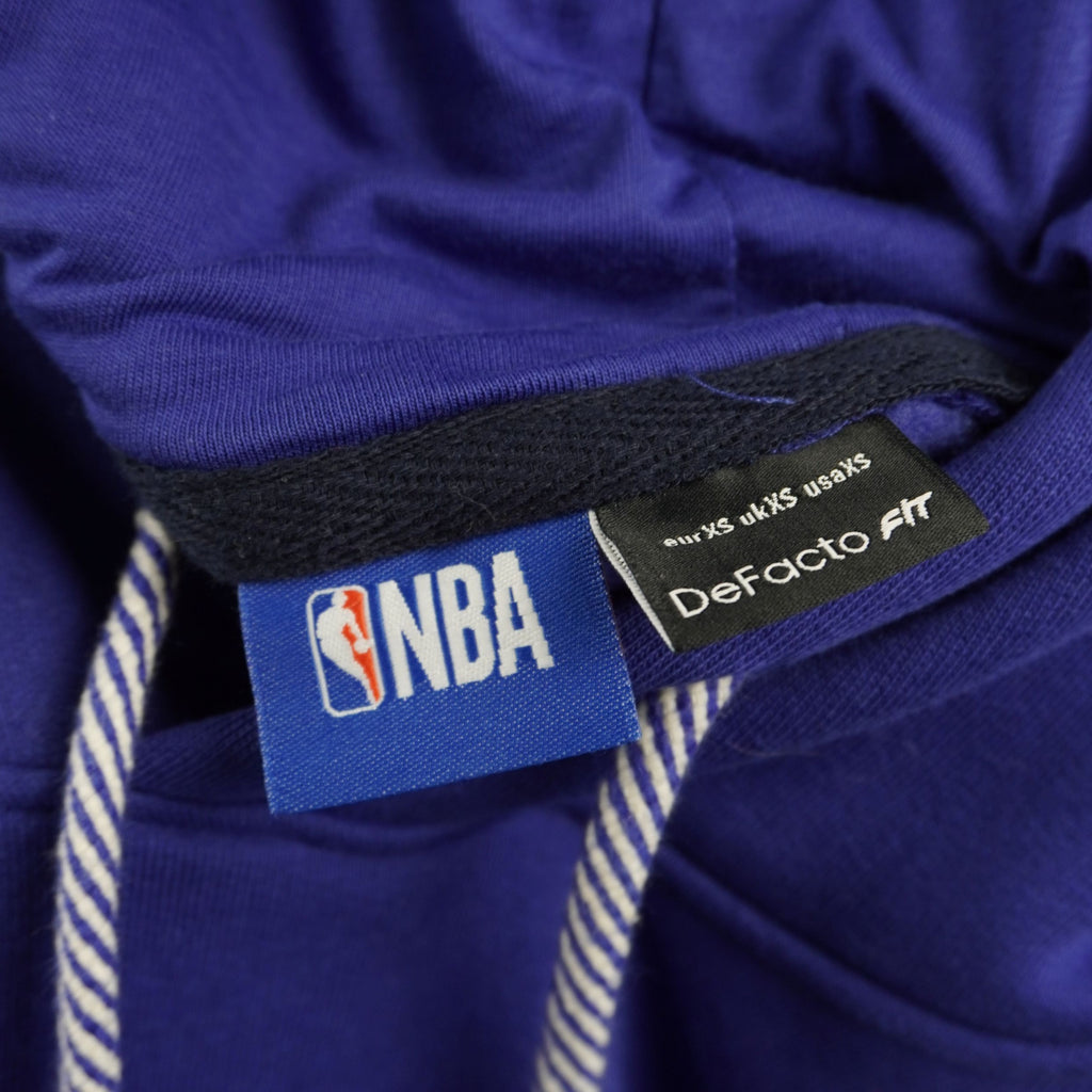 Primo piano dell'etichetta interna cucita sul collo con il logo ufficiale NBA e il brand DeFacto Fit.