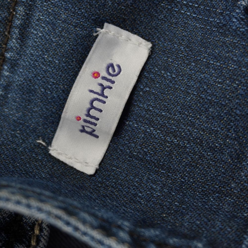 Etichetta interna in tessuto bianco satinato con logo ricamato in lettere minuscole blu e punti colorati del marchio d'archivio Pimkie.