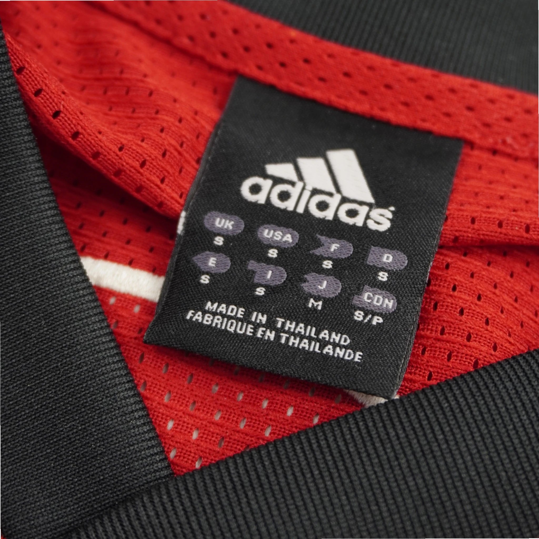 Dettaglio etichetta interna collo con taglie internazionali S e brand Adidas