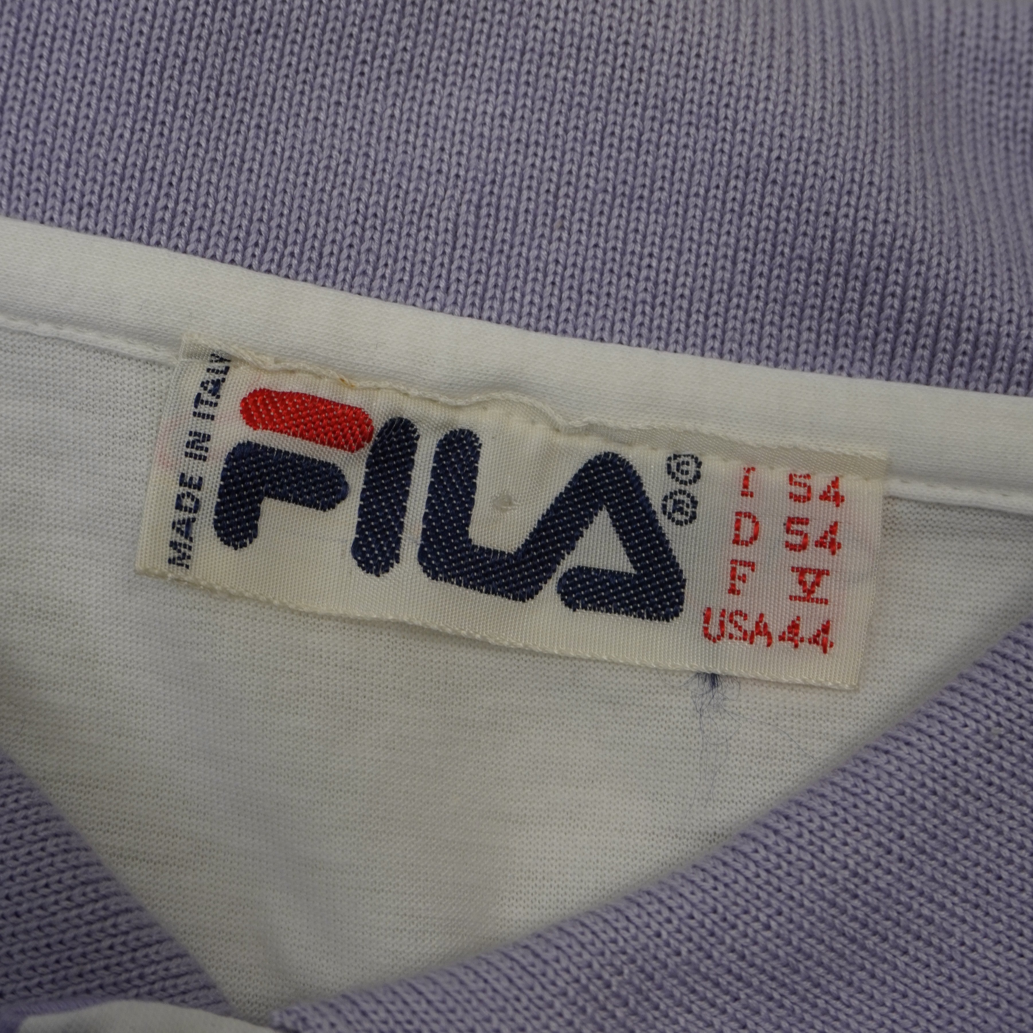 Primo piano dell'etichetta storica del colletto di una polo Fila vintage con la scritta Made in Italy, il logo rosso e blu e i dettagli delle taglie internazionali con il codice italiano 54.