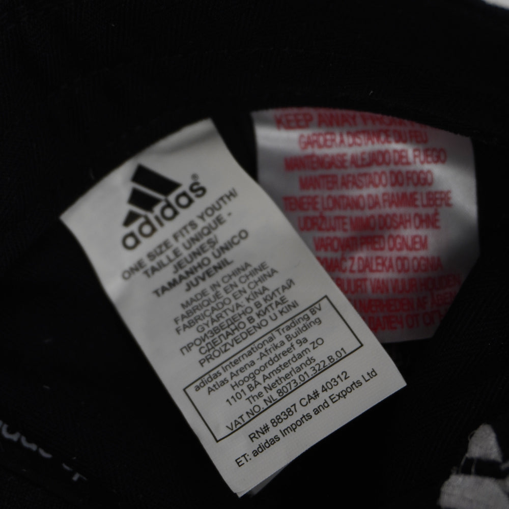 Primo piano del cartellino interno Adidas con indicazione del tessuto 100% cotone e istruzioni internazionali per la cura del capo.