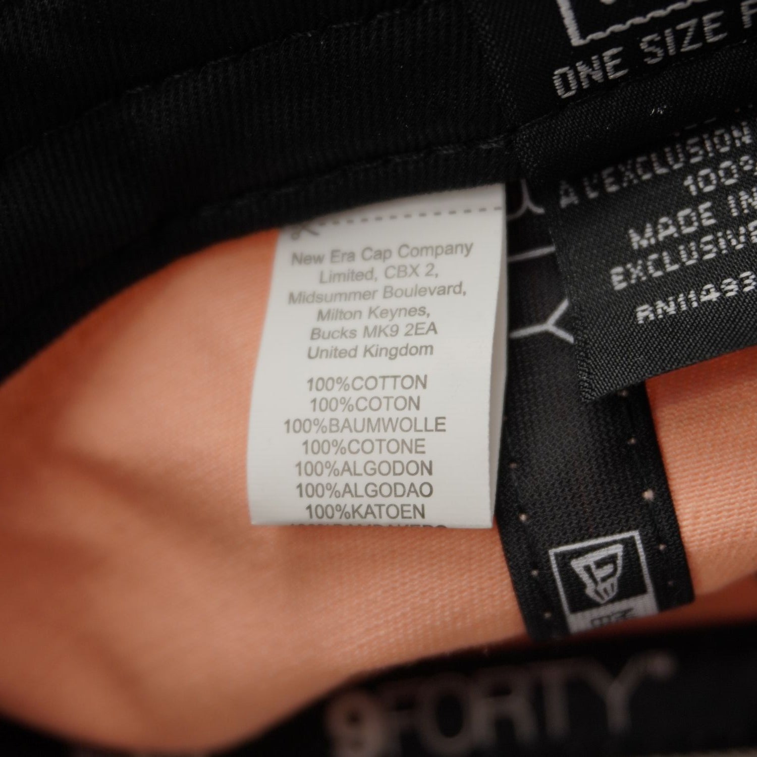 Etichetta interna nera di manutenzione New Era con indicazione tessuto 100% cotone, taglia One Size Fits Most e Made in Bangladesh.