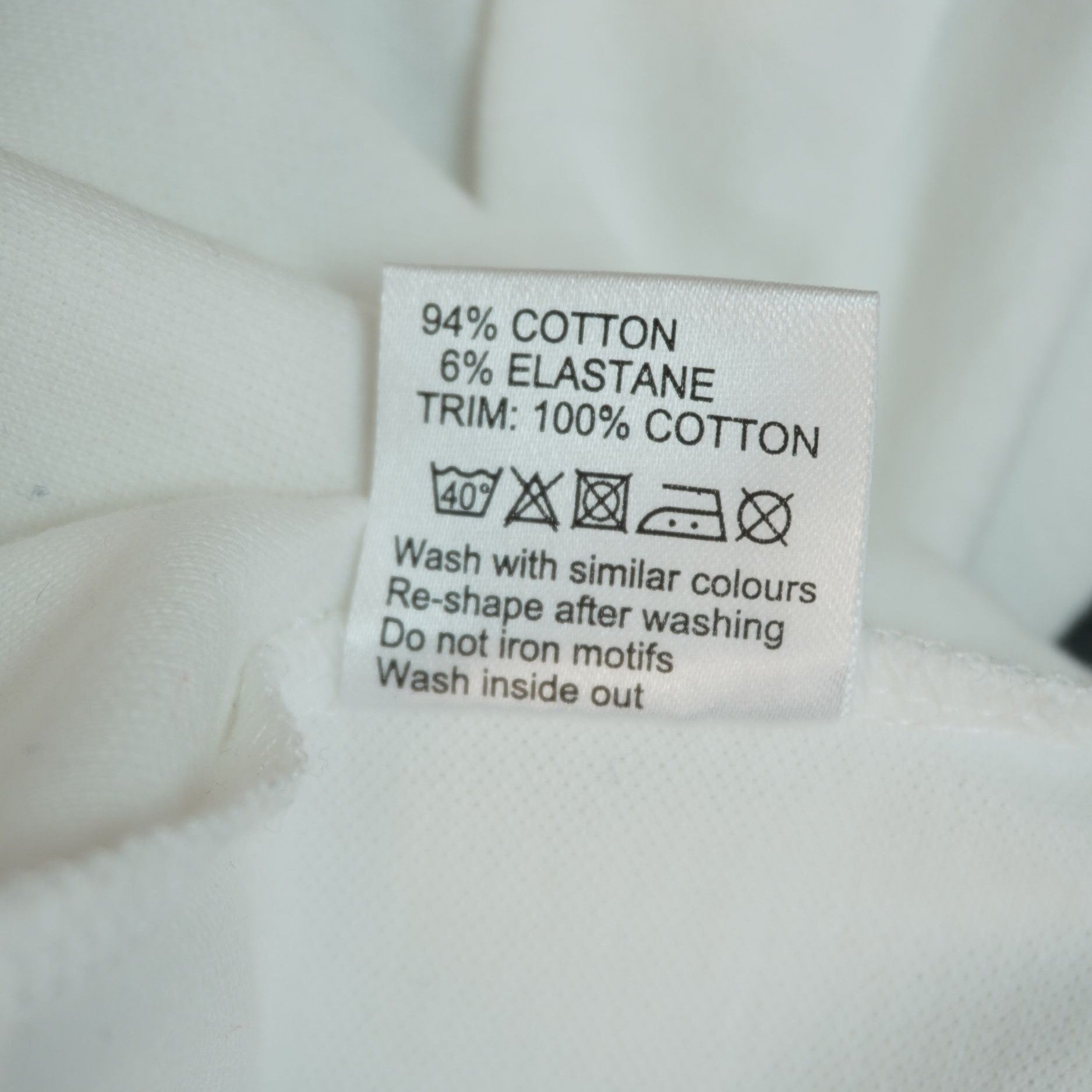 Etichetta interna di lavaggio che indica la composizione in 94% cotone e 6% elastane del corpo del capo.