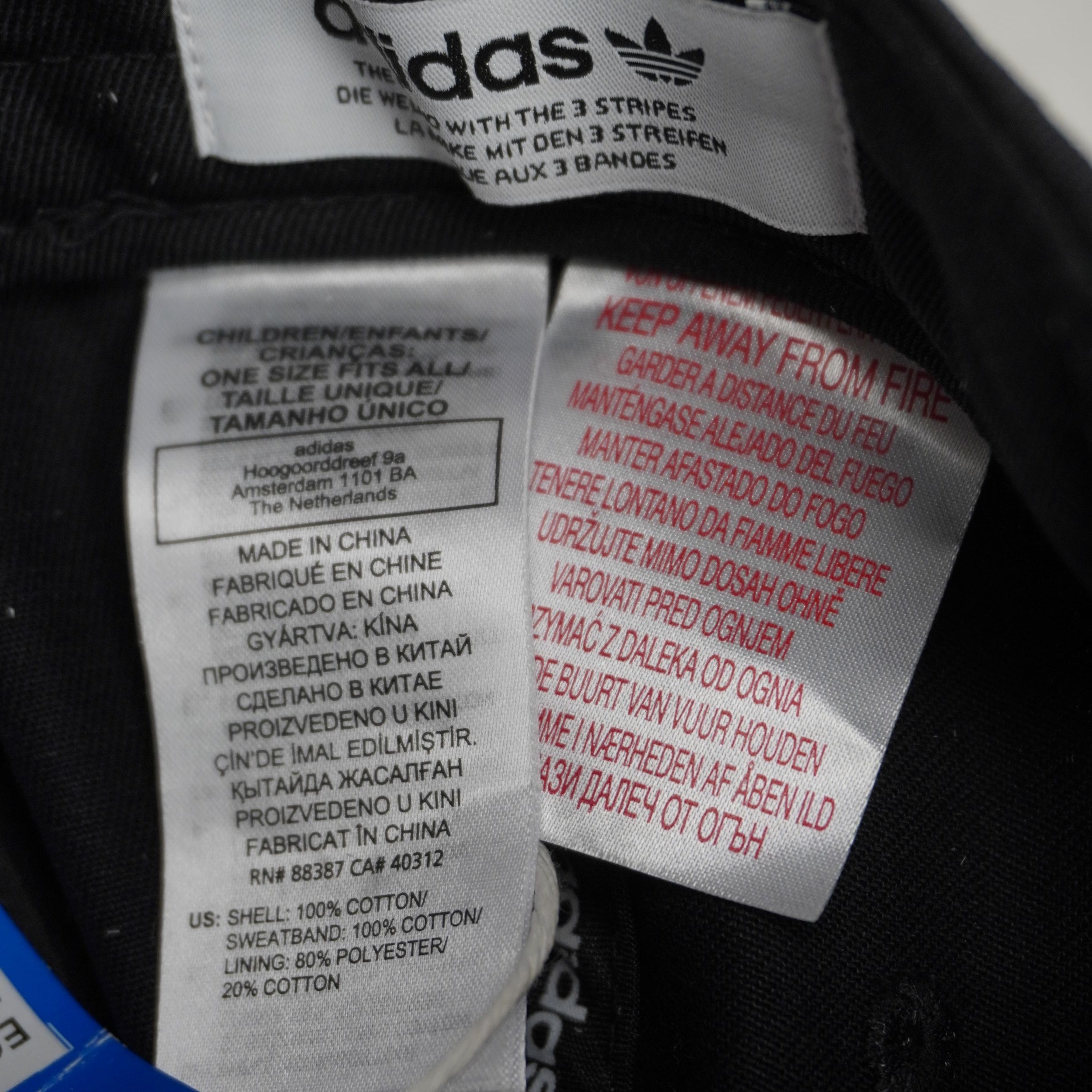 Primo piano dell'etichetta interna in tessuto della linea Adidas Originals che attesta la taglia Children One Size e la composizione.