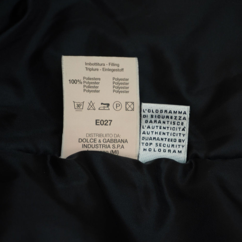 Primo piano delle etichette interne in tessuto chiaro che riportano la composizione dei materiali, il codice modello E027 e le istruzioni di lavaggio.