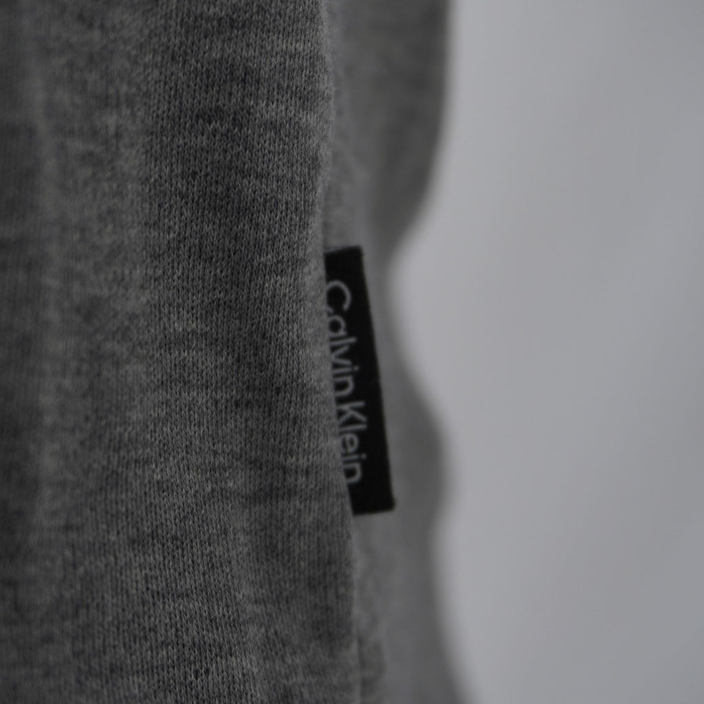 Dettaglio della flag label nera con scritta verticale Calvin Klein cucita sul fianco laterale della polo