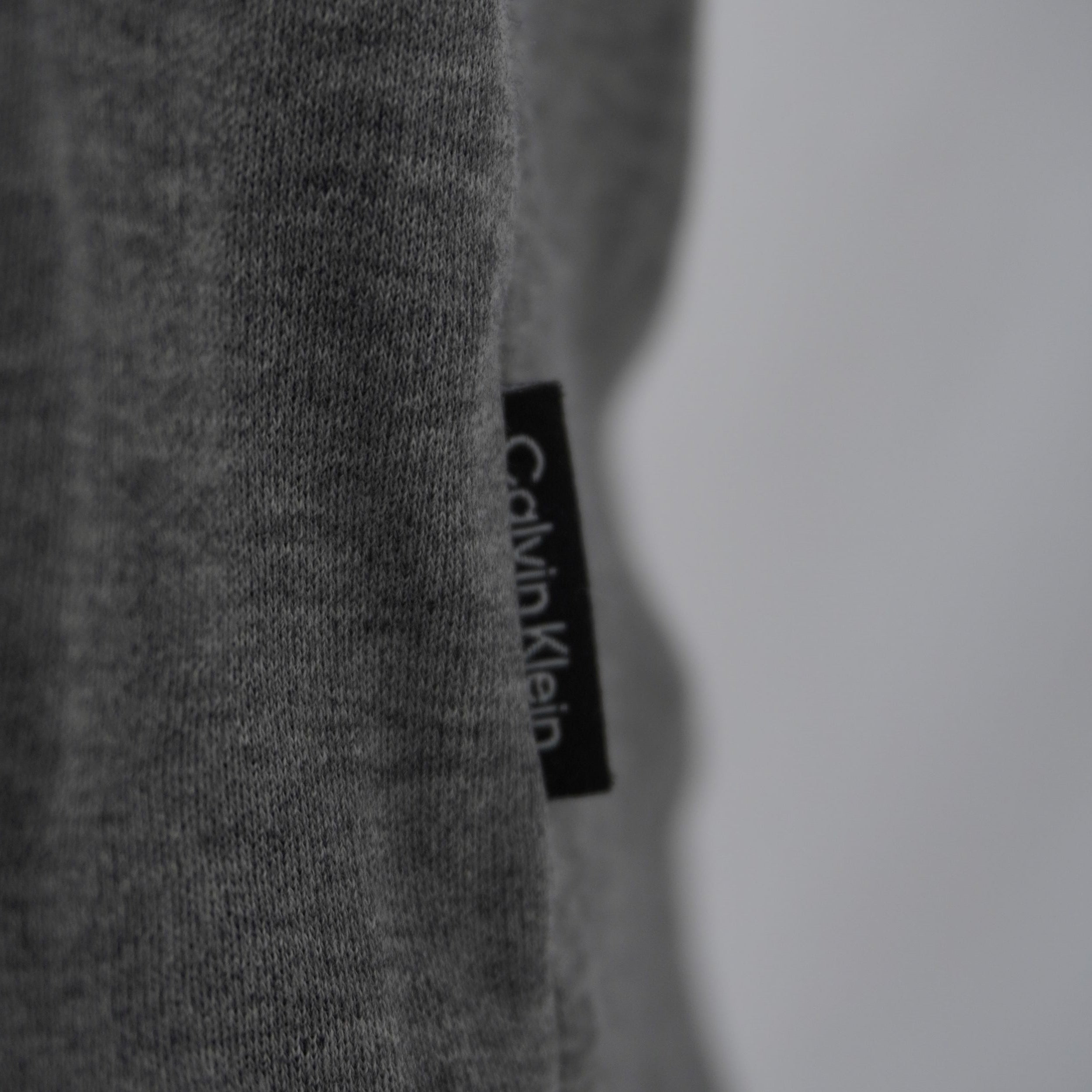 Dettaglio della flag label nera con scritta verticale Calvin Klein cucita sul fianco laterale della polo