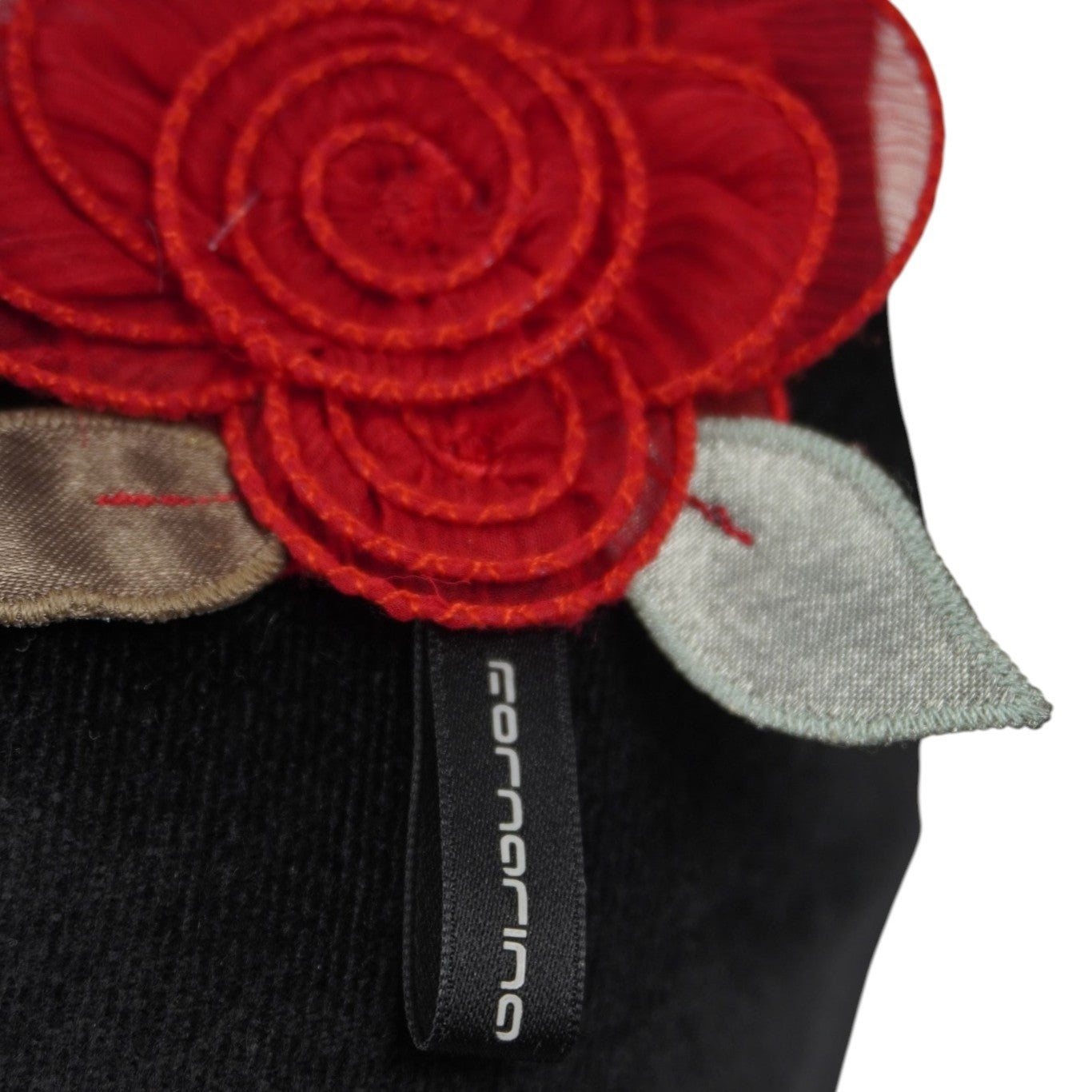 Particolare del logo Fornarina inciso su una placchetta metallica posizionata sotto la rosa decorativa.