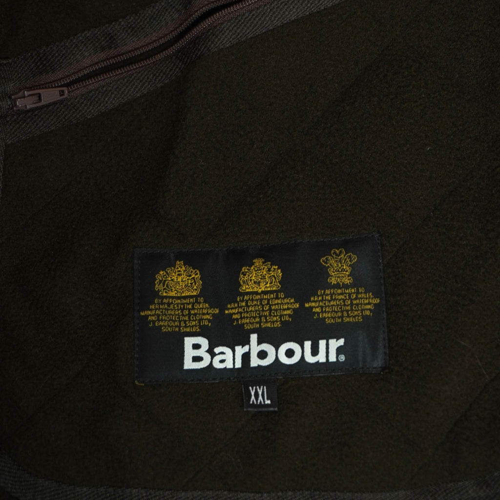 Primo piano dell'etichetta interna in tessuto nero con i tre loghi della casa reale britannica che attesta l'autenticità del capo Barbour.