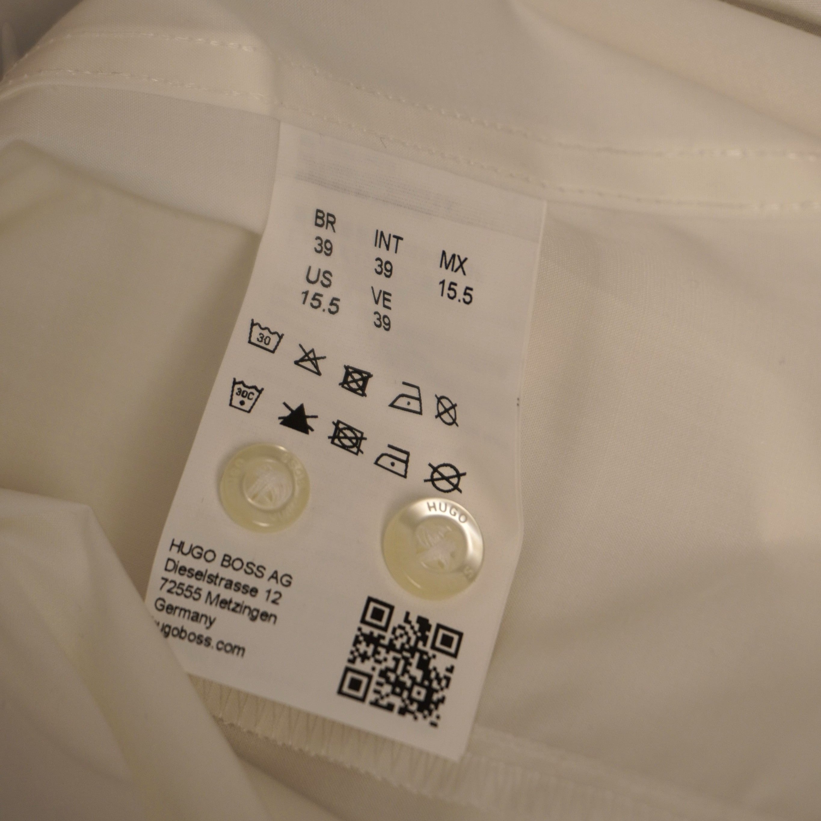  Inquadratura dell'etichetta interna in tessuto bianco stampata con i simboli di lavaggio e un codice QR per verificare l'originalità.
