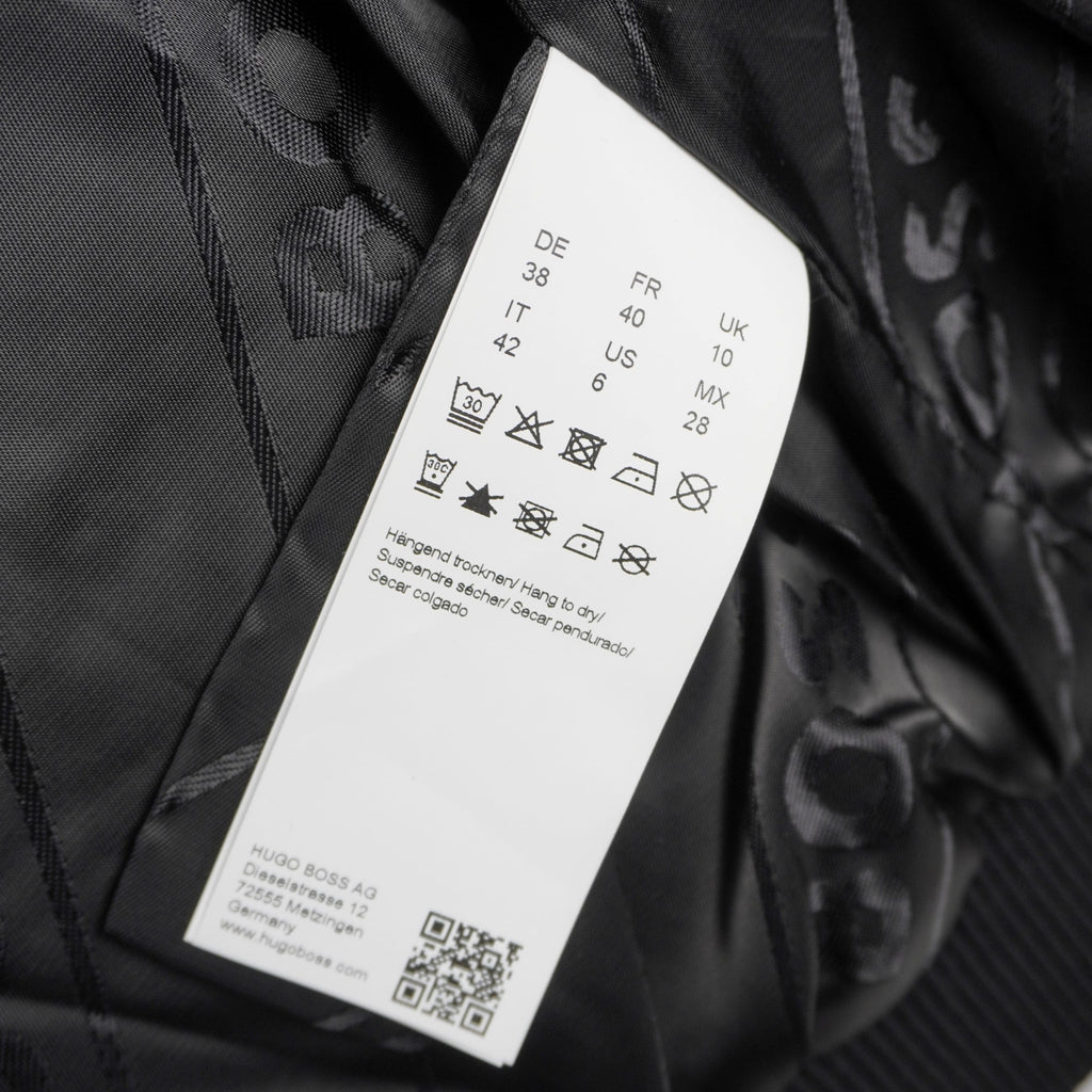 Inquadratura ravvicinata dell'etichetta interna bianca in tessuto satinato con i simboli di lavaggio, la composizione del materiale e un codice QR.