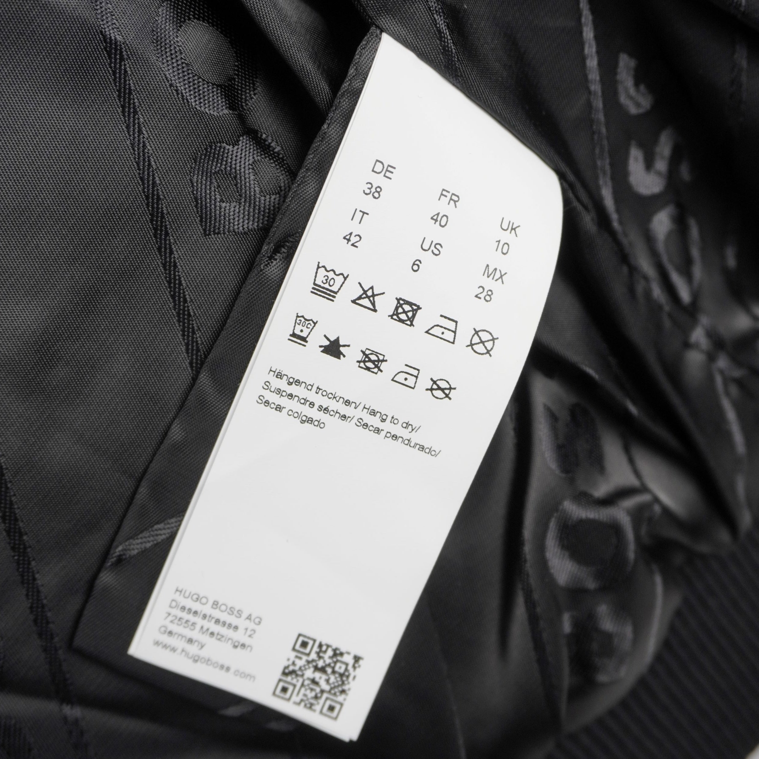 Inquadratura ravvicinata dell'etichetta interna bianca in tessuto satinato con i simboli di lavaggio, la composizione del materiale e un codice QR.