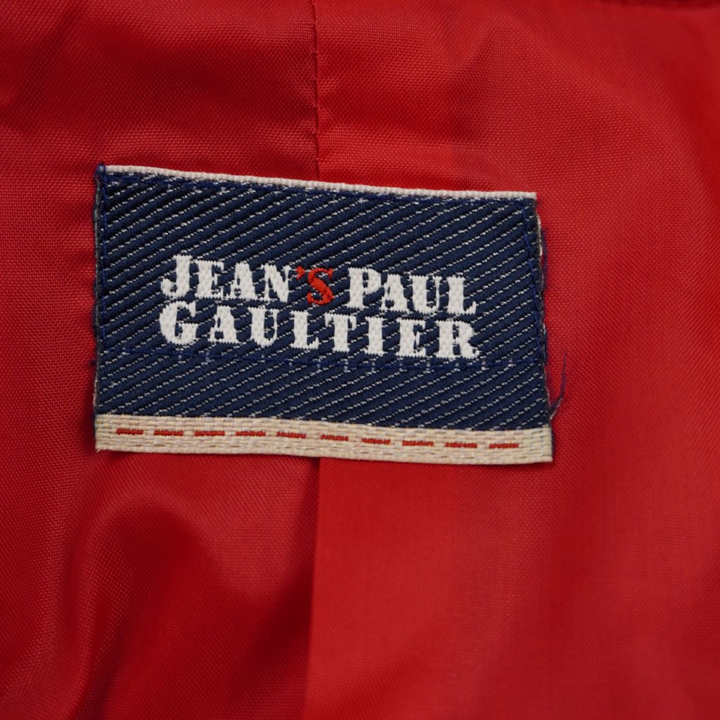 Dettaglio dell'etichetta rettangolare in tessuto blu originale Jeans Paul Gaultier cucita sulla fodera rossa interna.