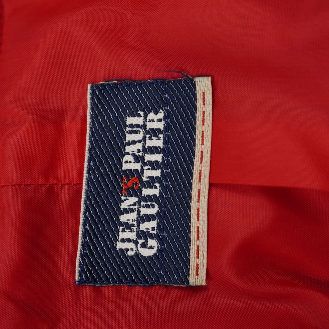 Dettaglio dell'etichetta rettangolare in tessuto blu originale Jeans Paul Gaultier cucita sulla fodera rossa interna.