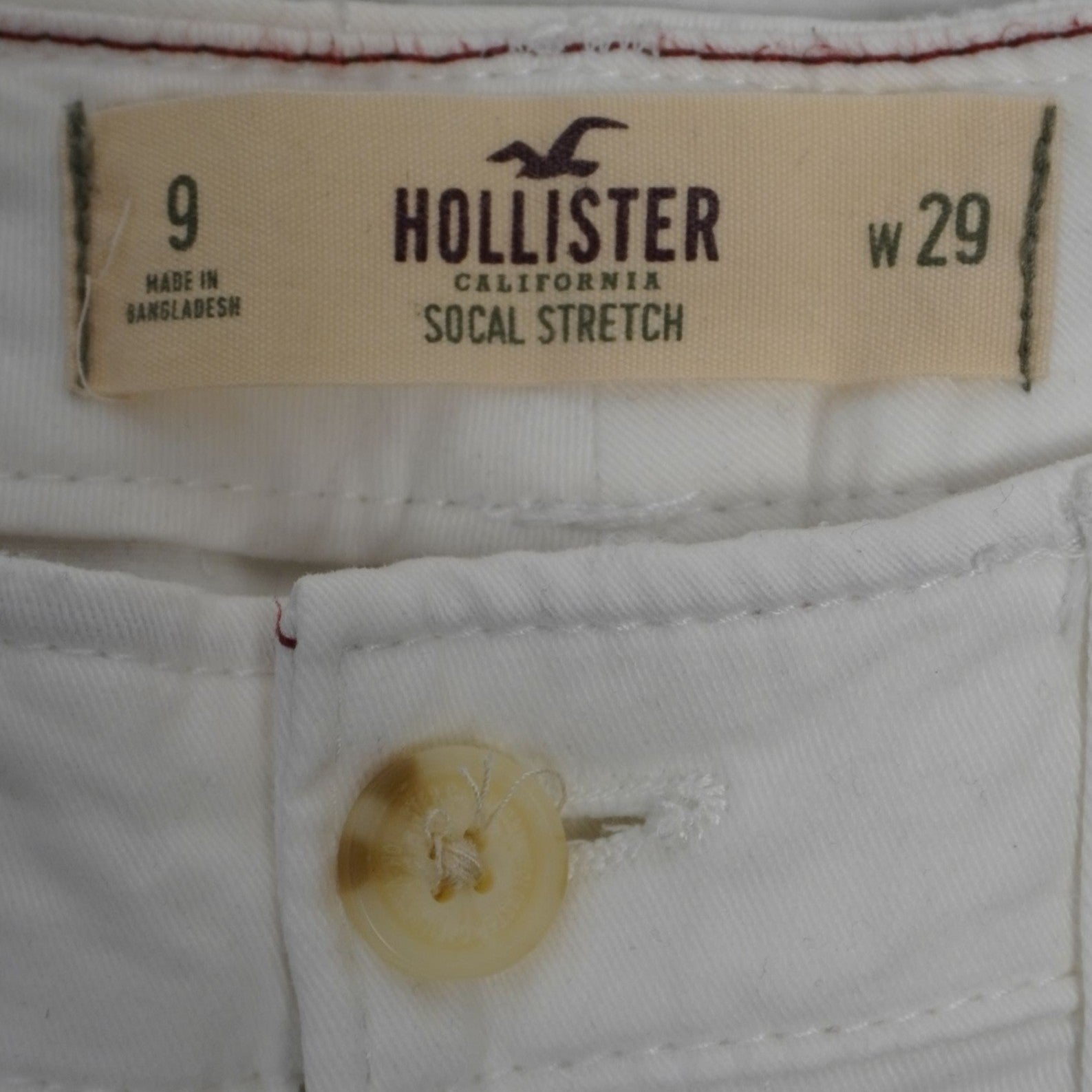 Primo piano dell'etichetta beige Hollister California SoCal Stretch taglia 9 W29 e del bottone frontale biondo.