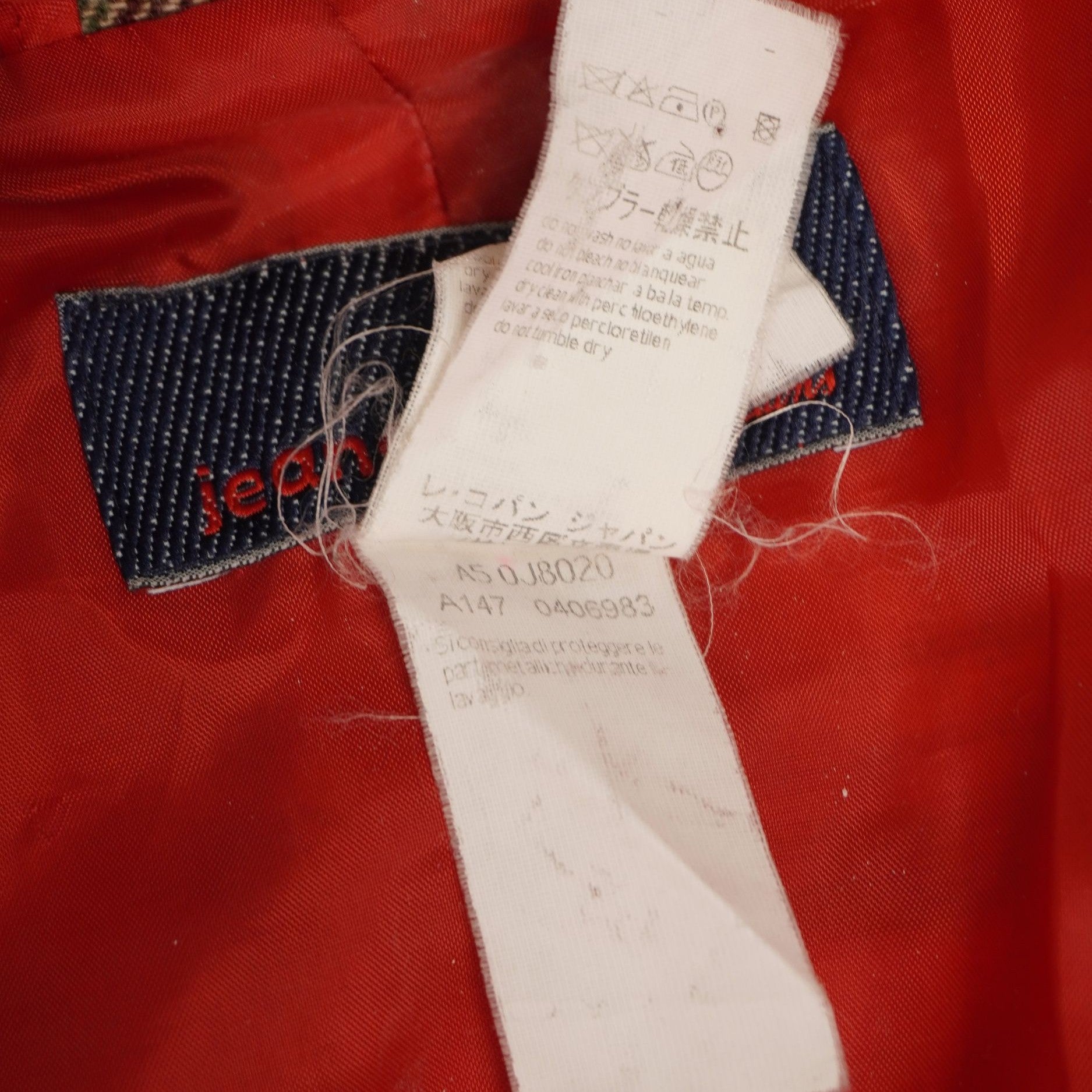 Inquadratura ravvicinata delle etichette interne di manutenzione fissate alla fodera rossa del cappotto scozzese.
