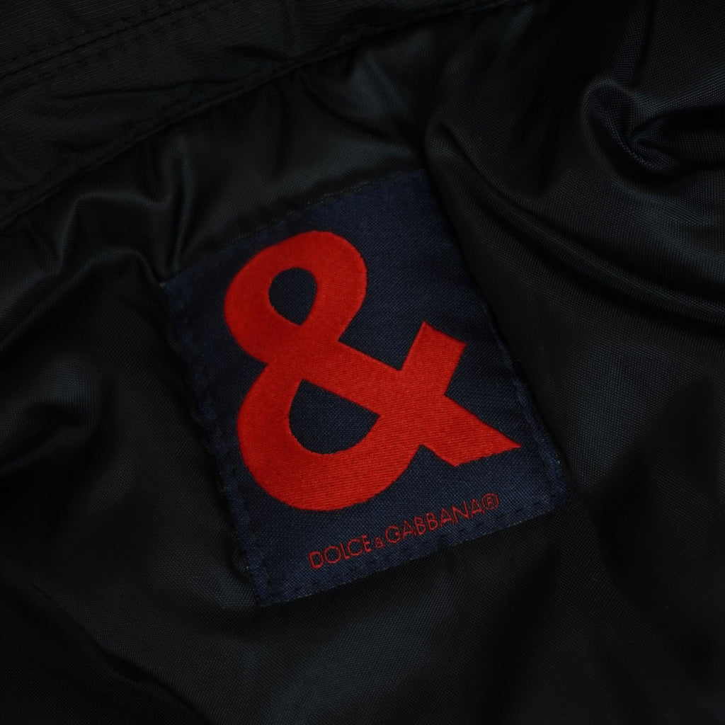 Primo piano dell'etichetta quadrata interna in tessuto blu scuro con il caratteristico logo "&" ricamato in rosso acceso.