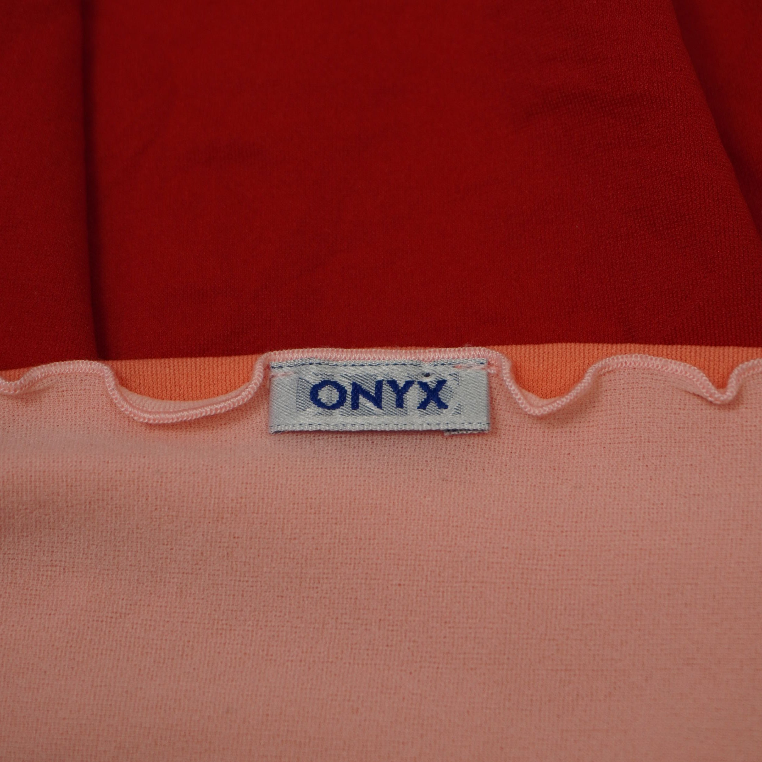 Primo piano dell'etichetta d'archivio originale con logo ONYX blu ricamato applicata sul bordo ondulato del corpetto.