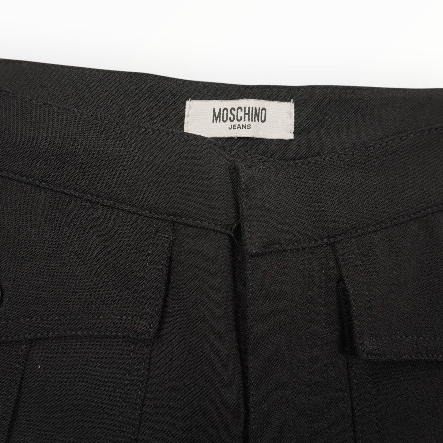 Primo piano del tag in tessuto bianco rettangolare con scritta nera Moschino Jeans applicato all'interno del girovita.