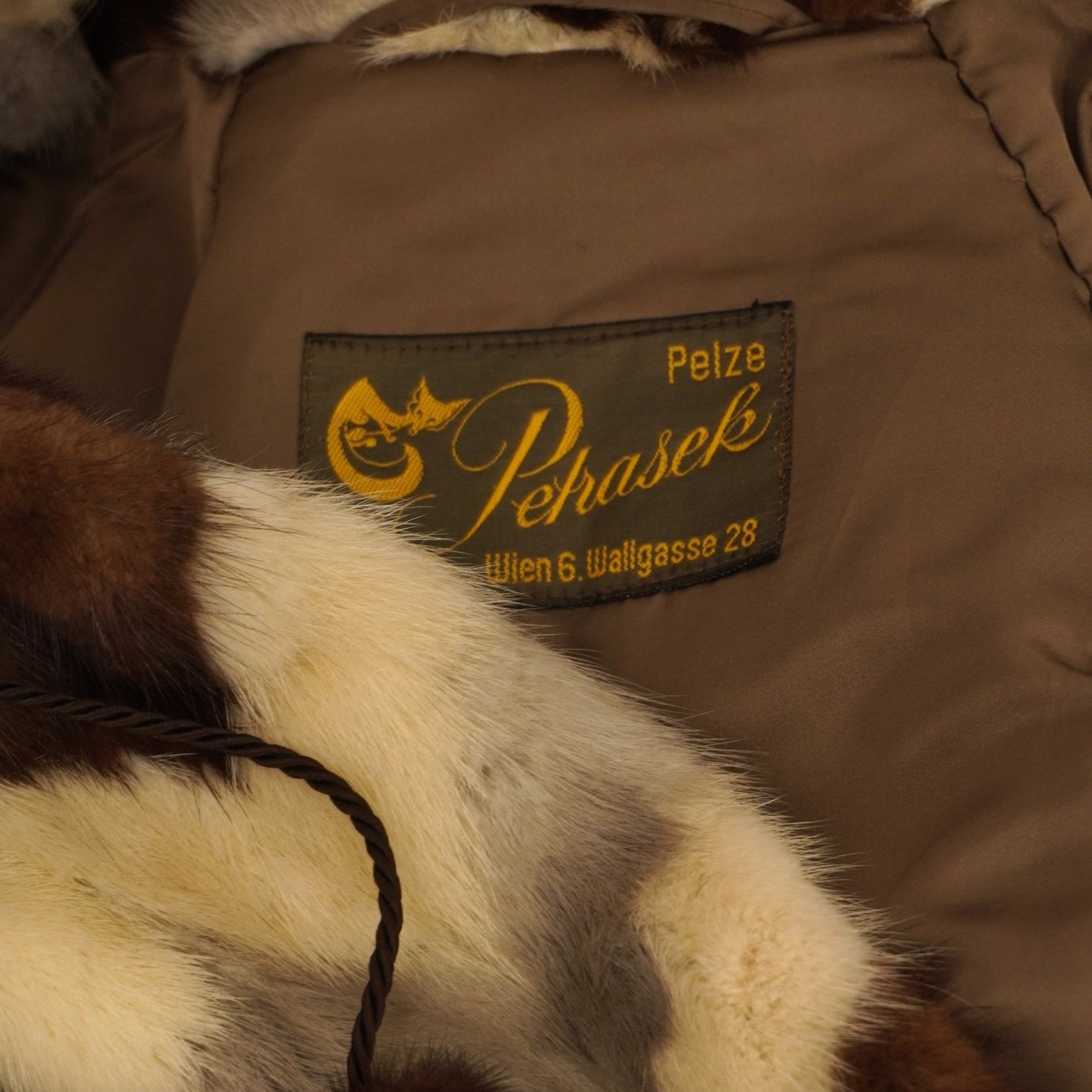 Primo piano dell'etichetta sartoriale dorata vintage Pelze Pehasek Wien cucita sulla fodera interna marrone della pelliccia.
