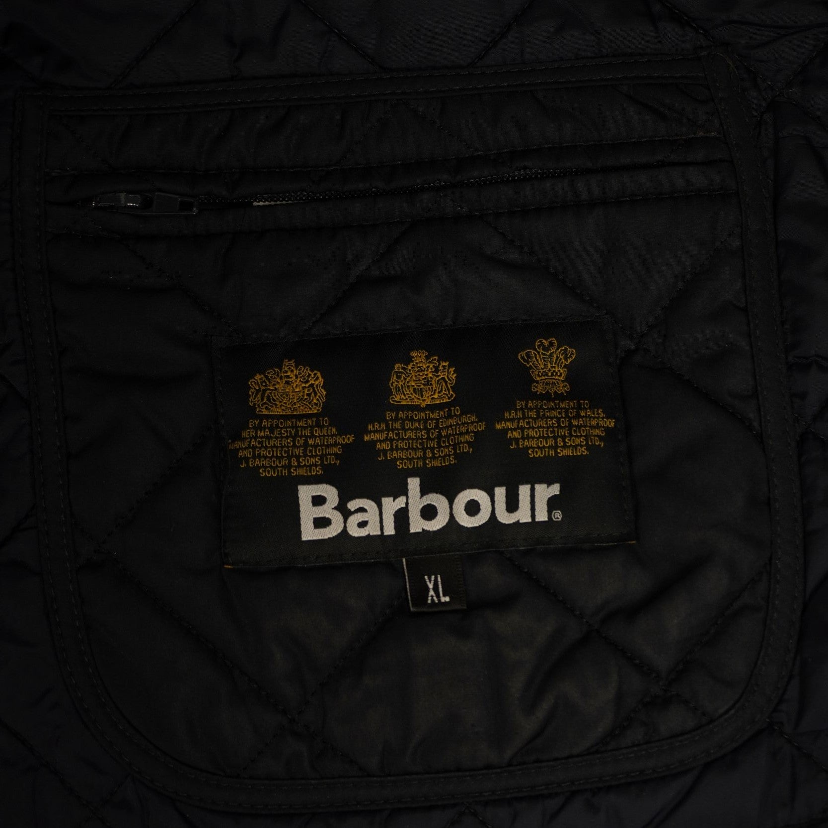 Dettaglio del logo Barbour dorato ricamato con i tre stemmi dei mandati reali ("Royal Warrants") sulla fodera interna nera.
