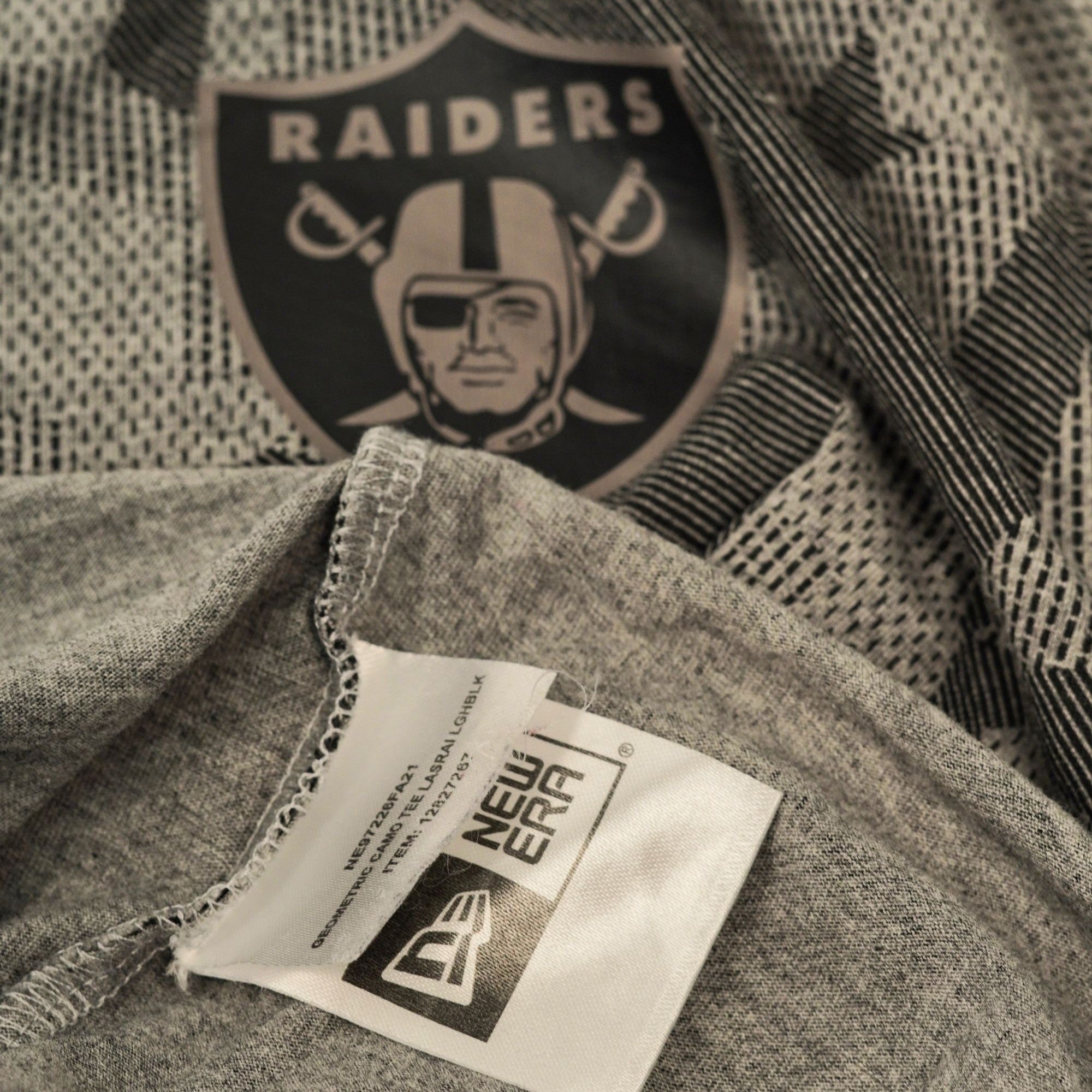 Dettaglio dello scollo interno che mostra l'etichetta nera stampata New Era e il logo dei Las Vegas Raiders cucito sul tessuto.