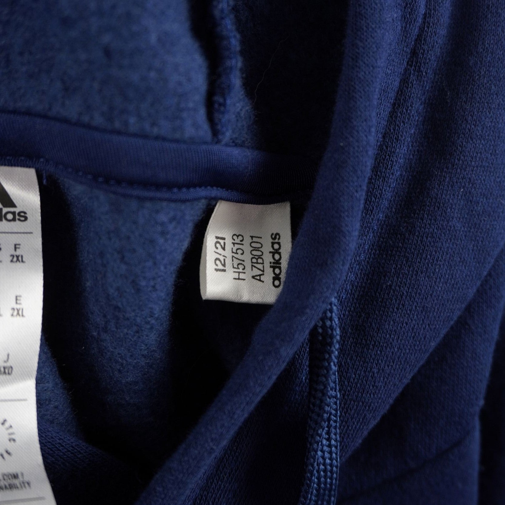 Dettaglio dell'etichetta interna bianca applicata sul collo della felpa adidas, che mostra le specifiche della taglia e l'autenticità del brand.