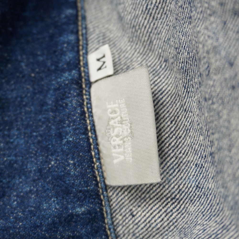 Primo piano dell'etichetta in tessuto grigio Versace Jeans Couture e del cartellino bianco della taglia M sotto il colletto.