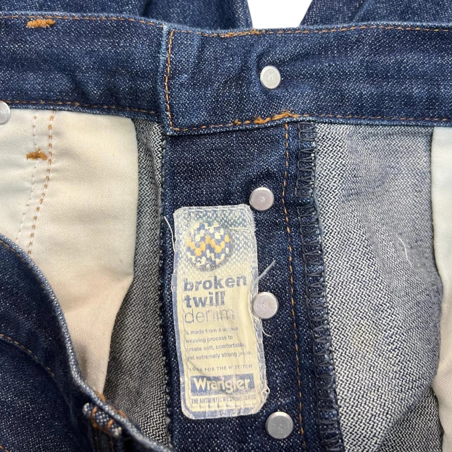 Etichetta gialla interna di un jeans Wrangler con indicazione della taglia 34-34 e 100% cotone