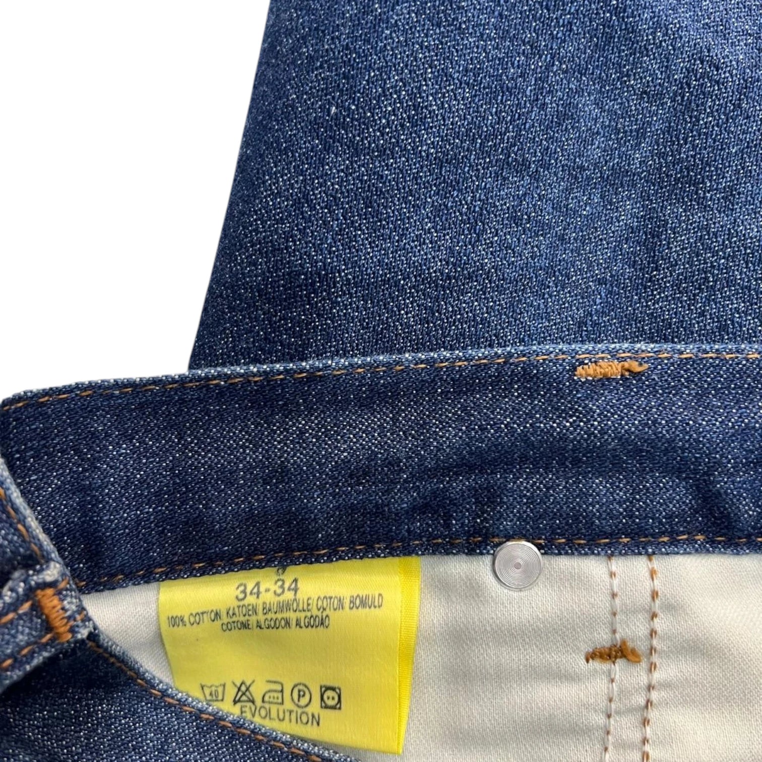 Etichetta gialla interna di un jeans Wrangler con indicazione della taglia 34-34 e 100% cotone