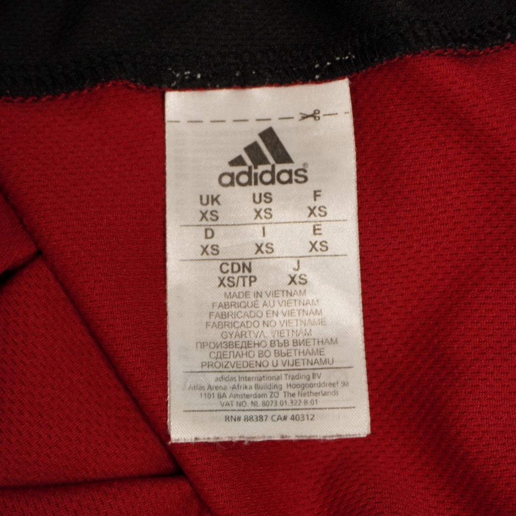 Dettaglio dell'etichetta interna quadrata in tessuto bianco con il logo Adidas e le indicazioni delle taglie internazionali.
