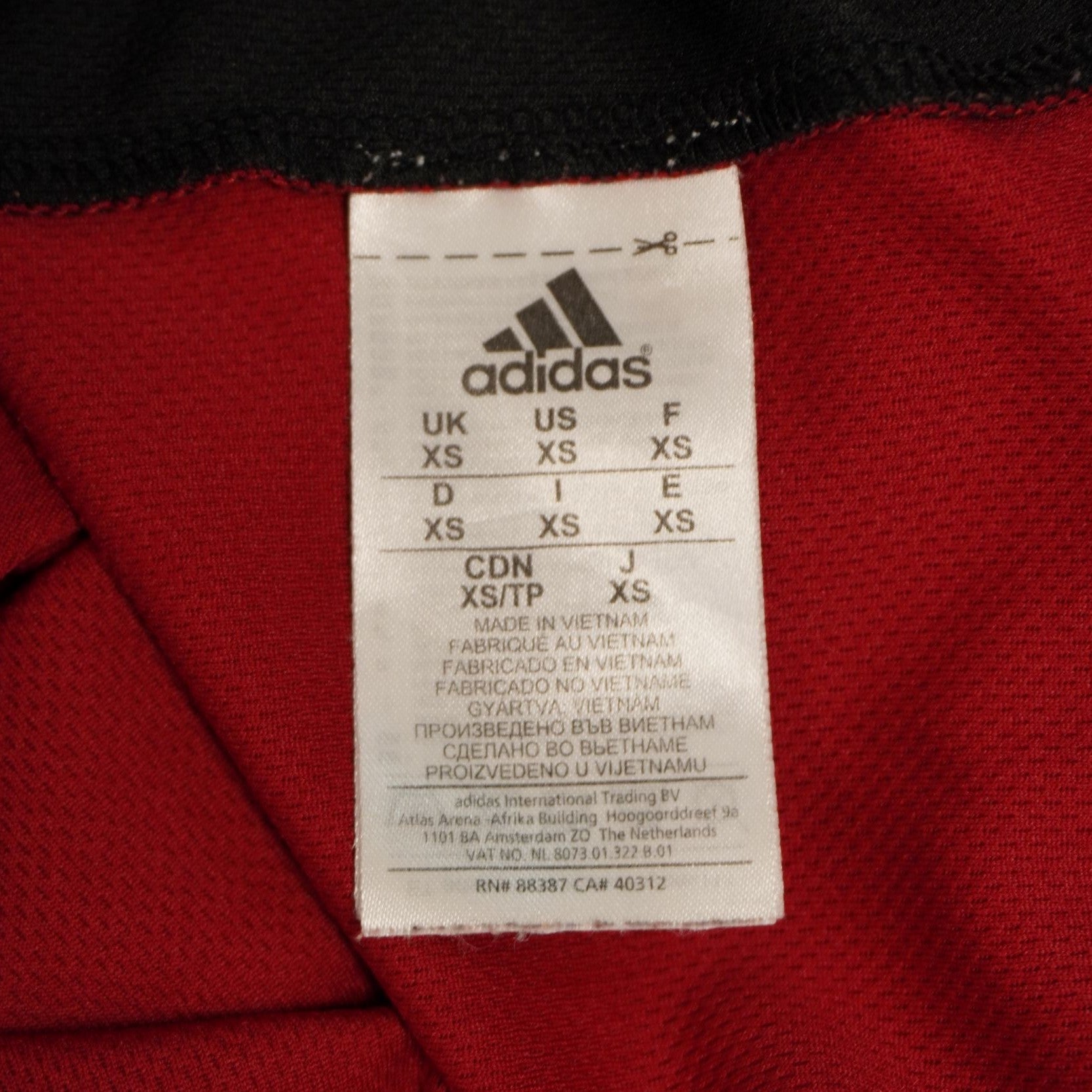 Dettaglio dell'etichetta interna quadrata in tessuto bianco con il logo Adidas e le indicazioni delle taglie internazionali.