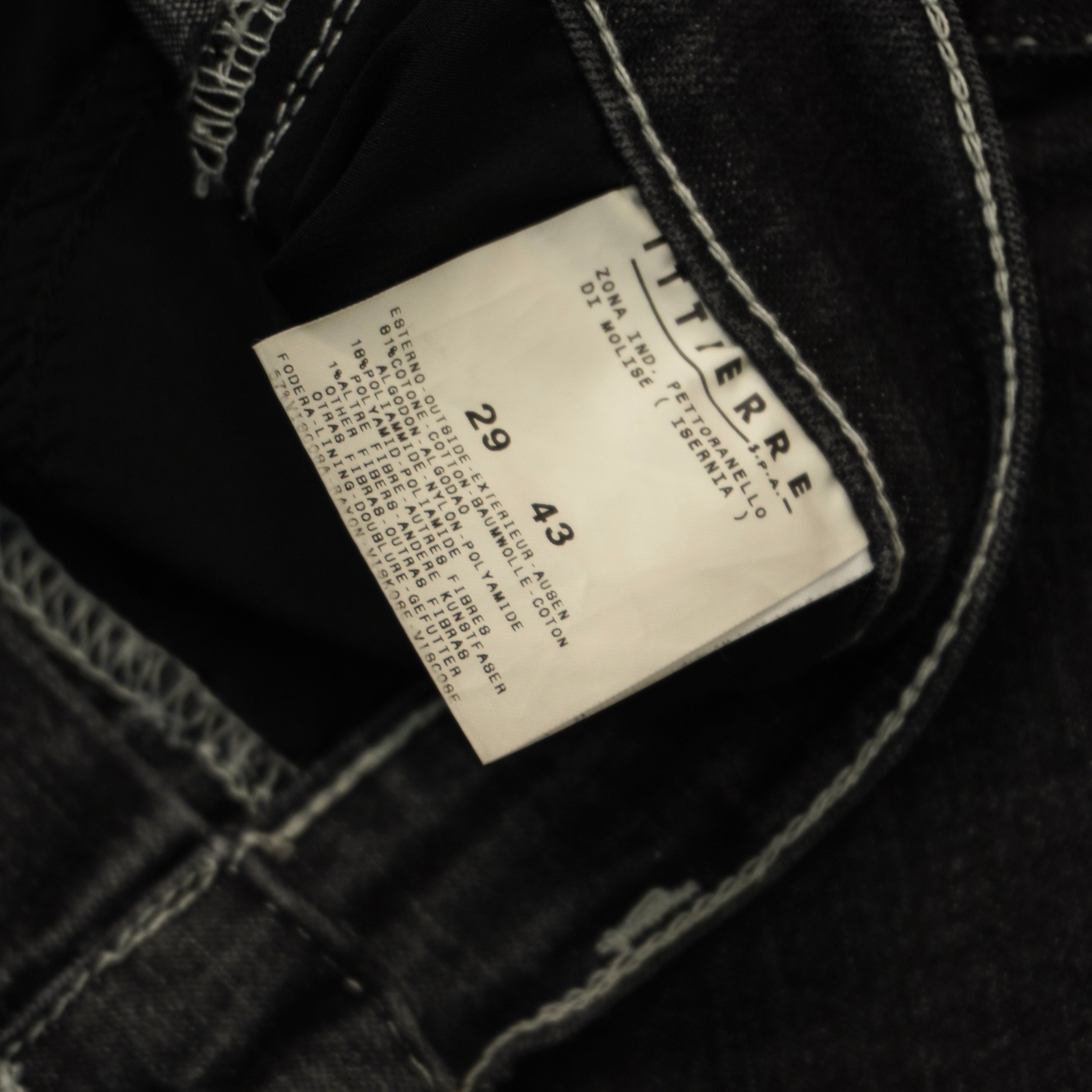 Primo piano del tag interno rettangolare bianco con scritta nera Versace Jeans Couture e indicazione di taglia.