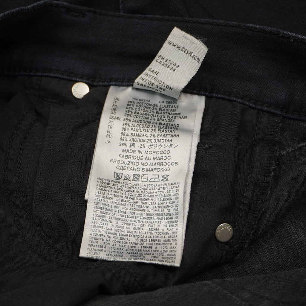 Dettaglio del cartellino interno bianco verticale con i simboli di manutenzione e lavaggio a 30 gradi del denim stretch.