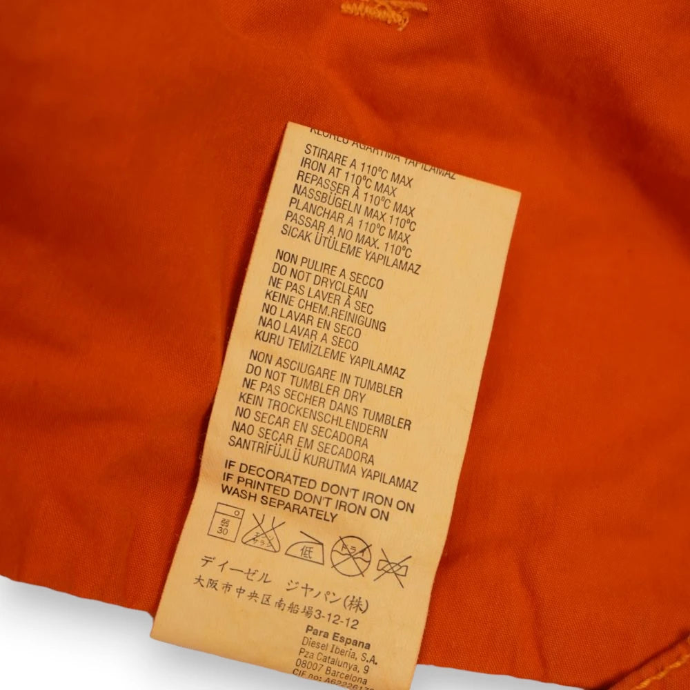 Etichetta interna bianca con le istruzioni di cura e lavaggio in diverse lingue dei pantaloni vintage Diesel arancioni.