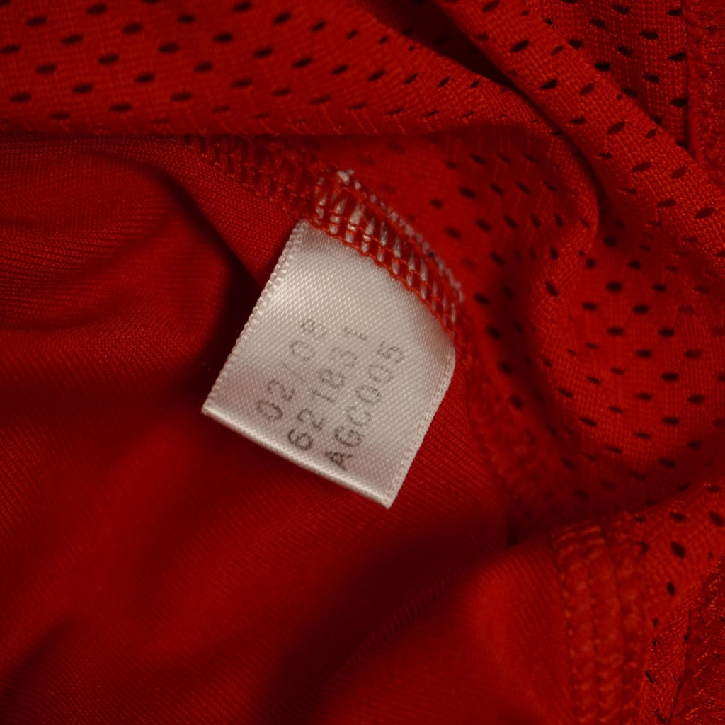 Etichetta bianca interna con le istruzioni e i simboli per il lavaggio e la cura del tessuto in poliestere della polo Adidas.
