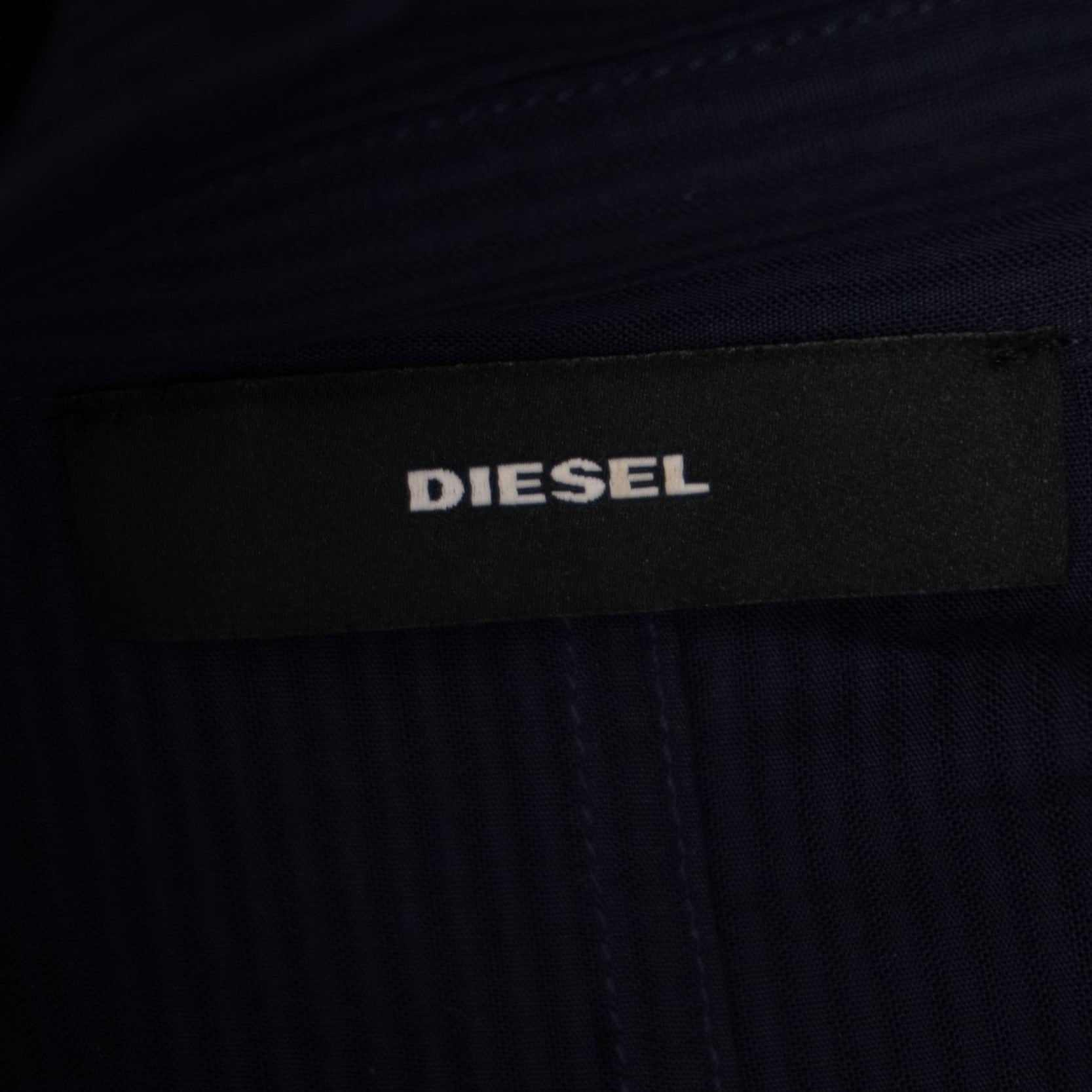 Inquadratura ravvicinata del logo Diesel scritto in bianco su una piccola etichetta rettangolare nera applicata sul capo.
