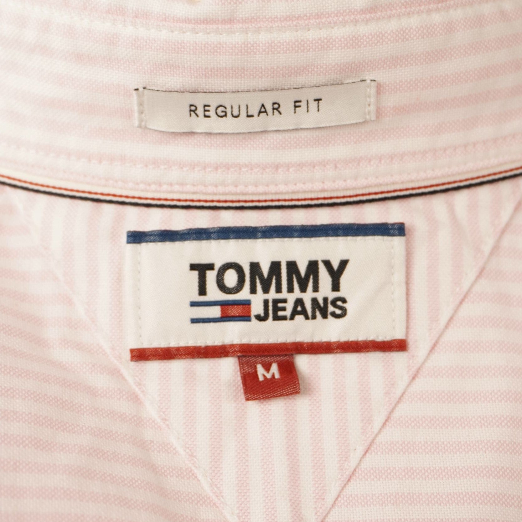 Dettaglio dell'etichetta interna rettangolare bianca Tommy Jeans con indicazione della taglia M.