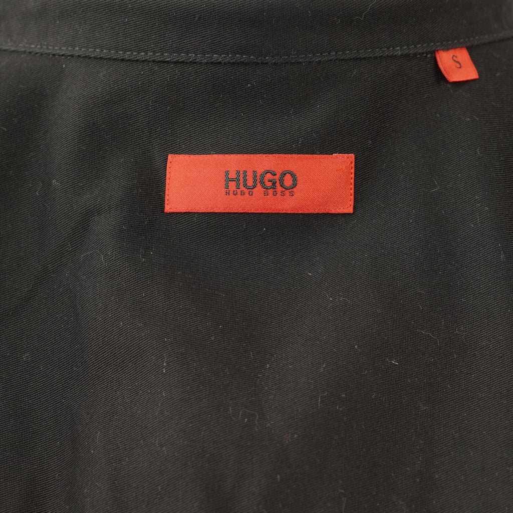 Particolare piatto dell'etichetta con logo rosso HUGO per la verifica dell'autenticità e dello stato del tessuto.