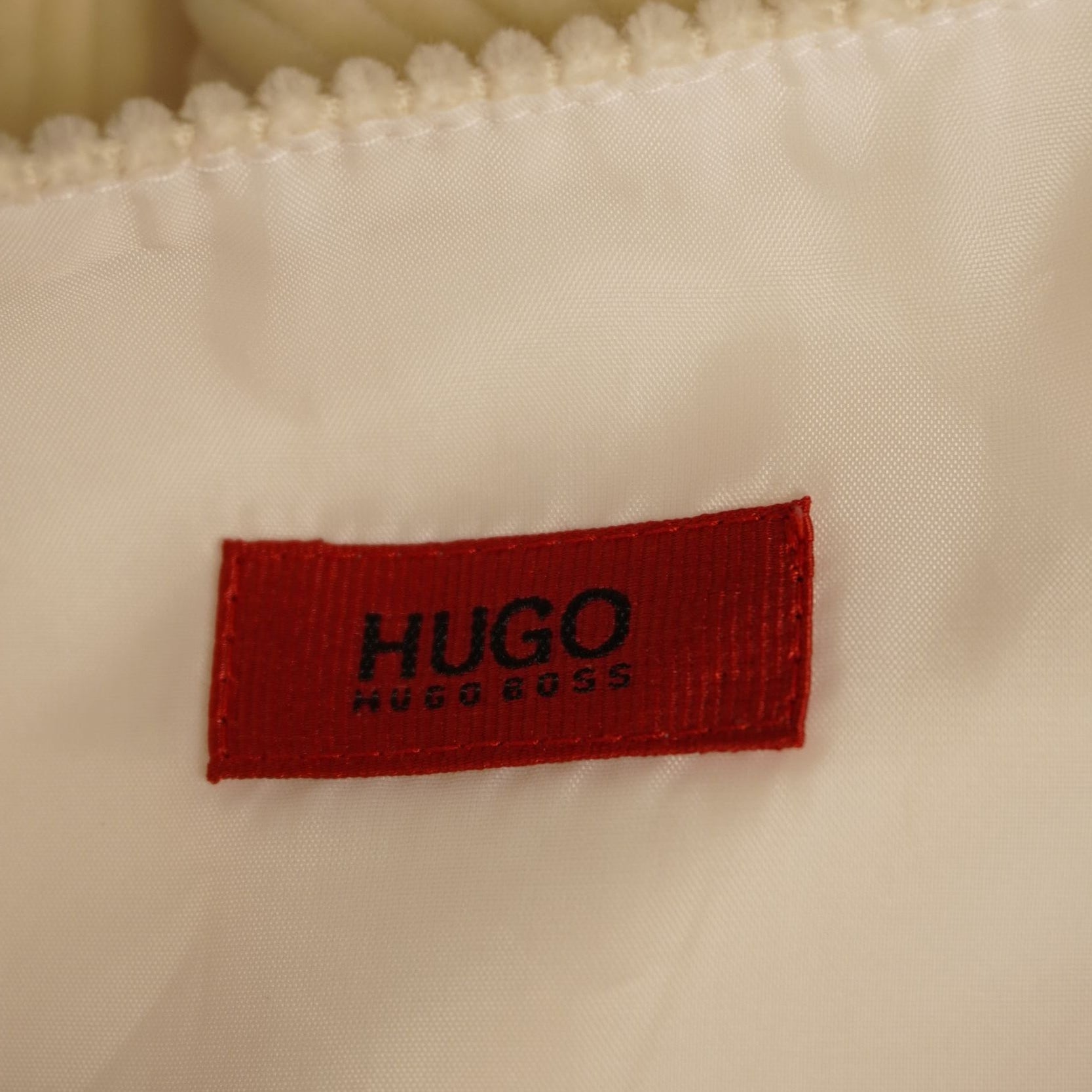 Dettaglio dell'etichetta interna rettangolare di colore rosso con il logo nero HUGO ricamato.