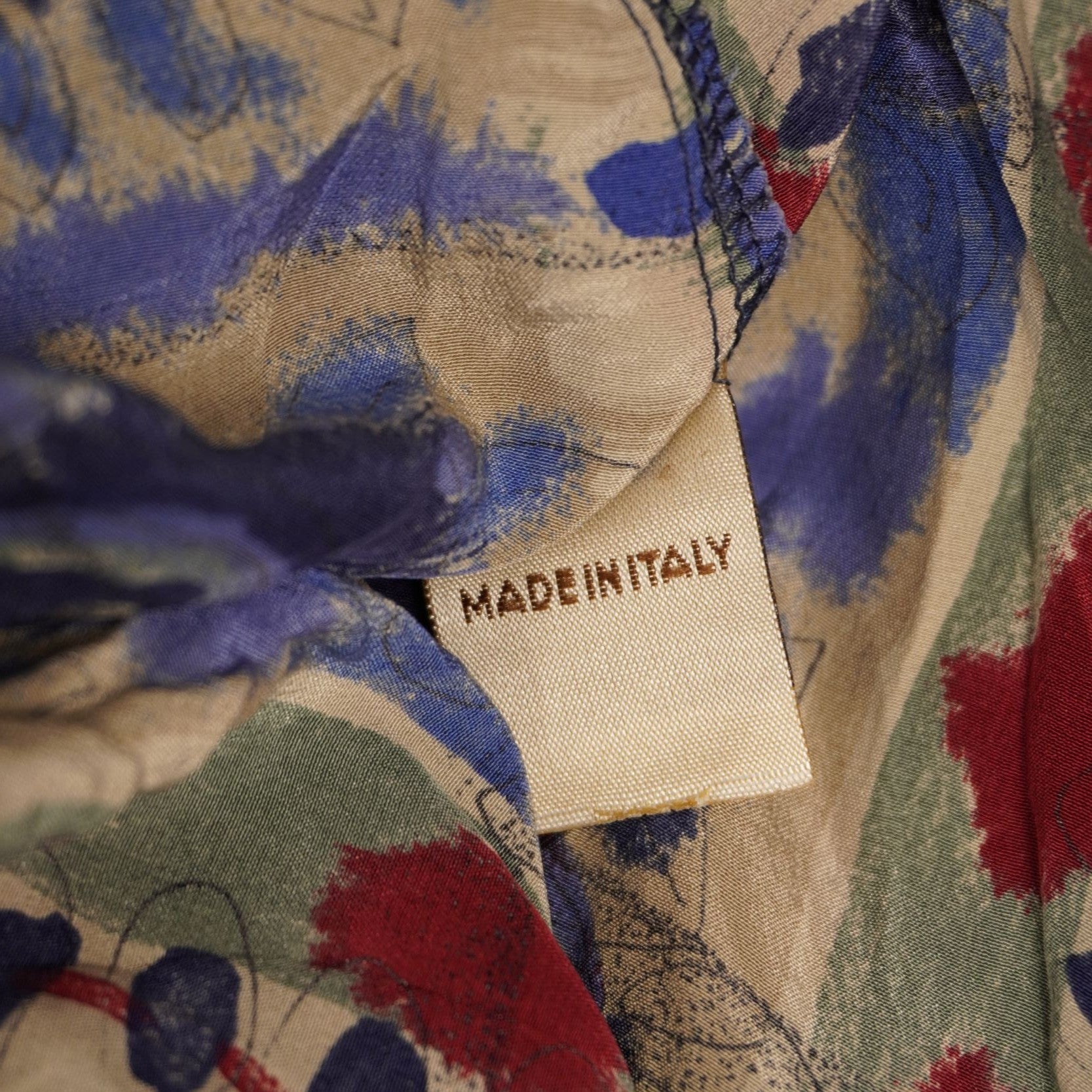 Primo piano del cartellino interno bianco con la scritta Made in Italy cucito sul tessuto colorato della camicia.