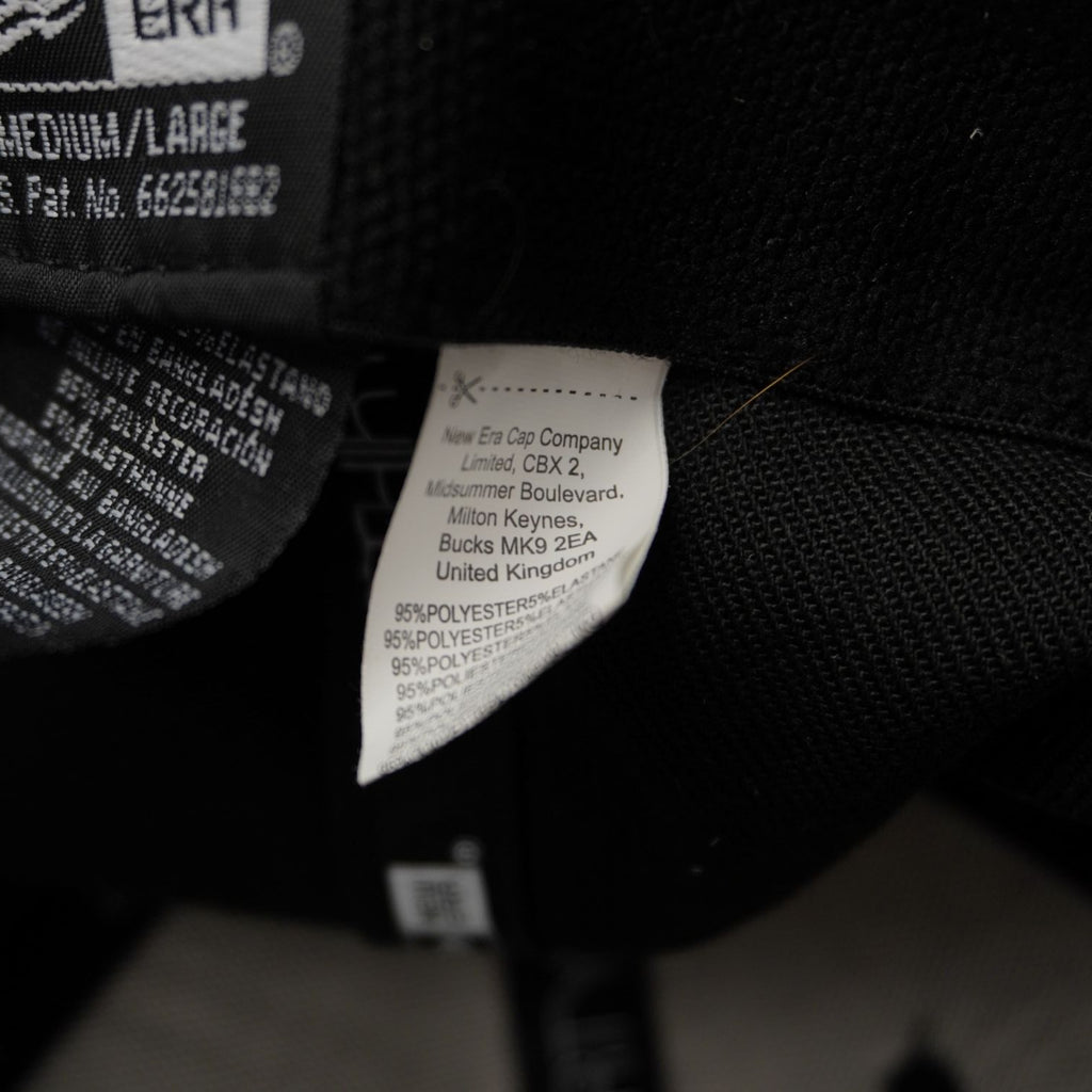 Etichetta interna di lavaggio e cura del cappellino New Era Cap Company Limited che indica la composizione in poliestere ed elastan.