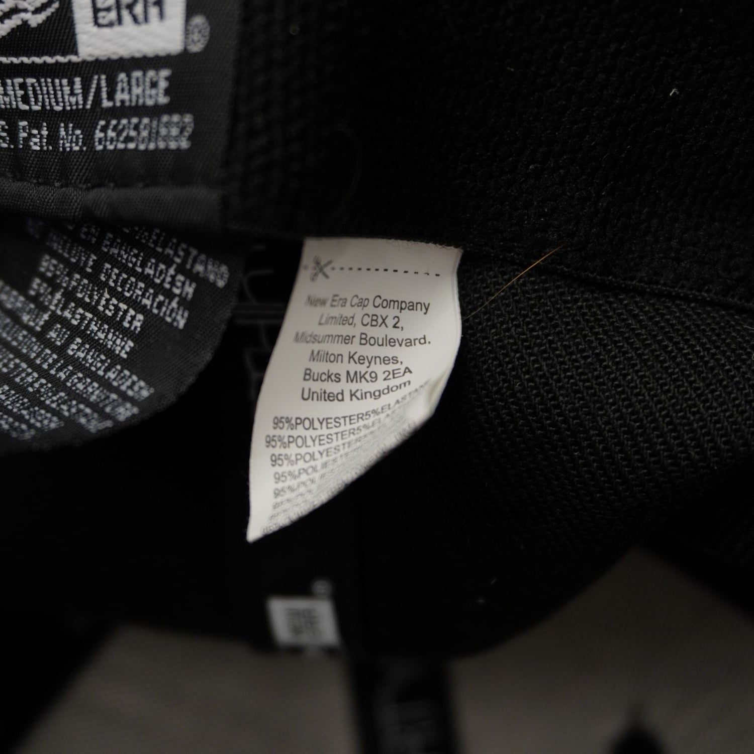 Etichetta interna di lavaggio e cura del cappellino New Era Cap Company Limited che indica la composizione in poliestere ed elastan.