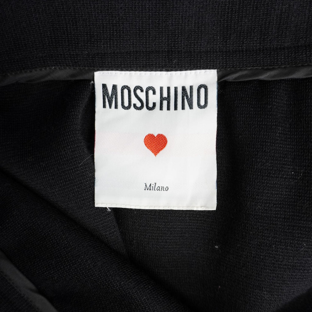  Primo piano dell'etichetta interna quadrata in tessuto bianco Moschino Cheap and Chic con l'iconico simbolo del cuore rosso.