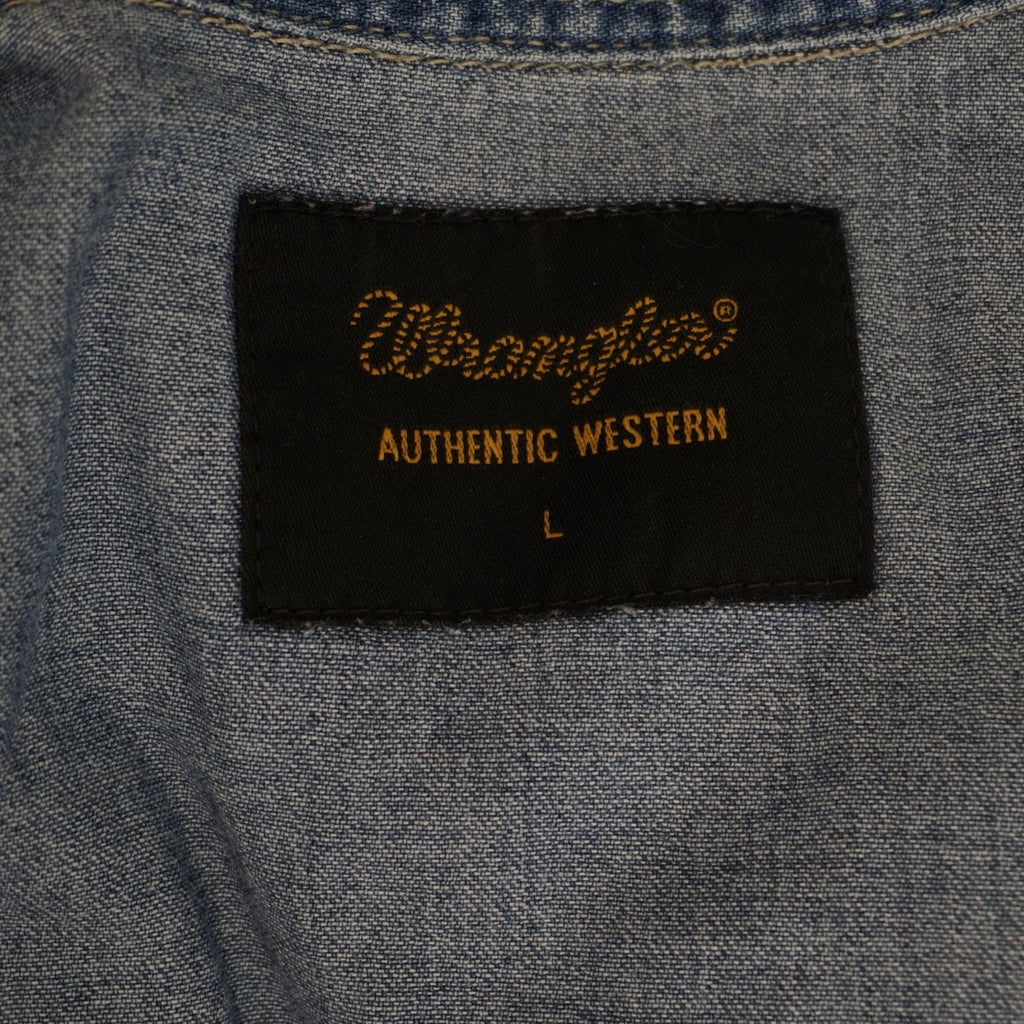 Inquadratura dell'etichetta rettangolare nera cucita sotto il colletto interno con la scritta dorata Wrangler Rugged Wear e la taglia L.