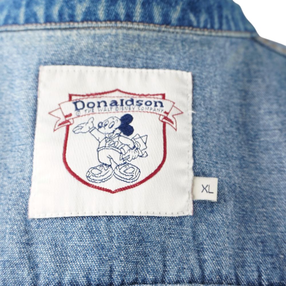Primo piano dell'etichetta interna in tessuto bianco Donaldson The Walt Disney Company con indicazione della taglia XL.