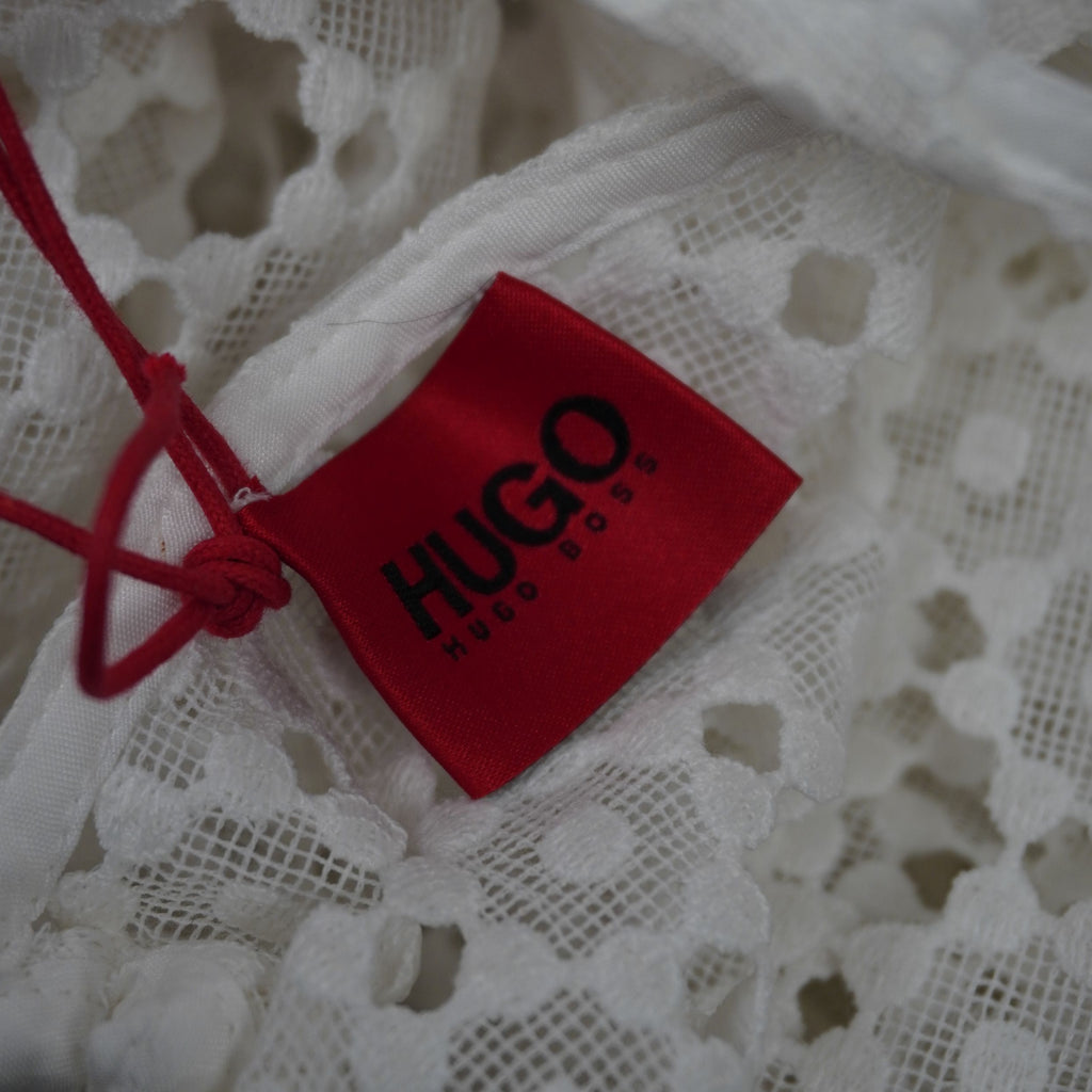 Cartellino rosso originale del brand HUGO Hugo Boss attaccato al tessuto traforato dell'abito bianco.
