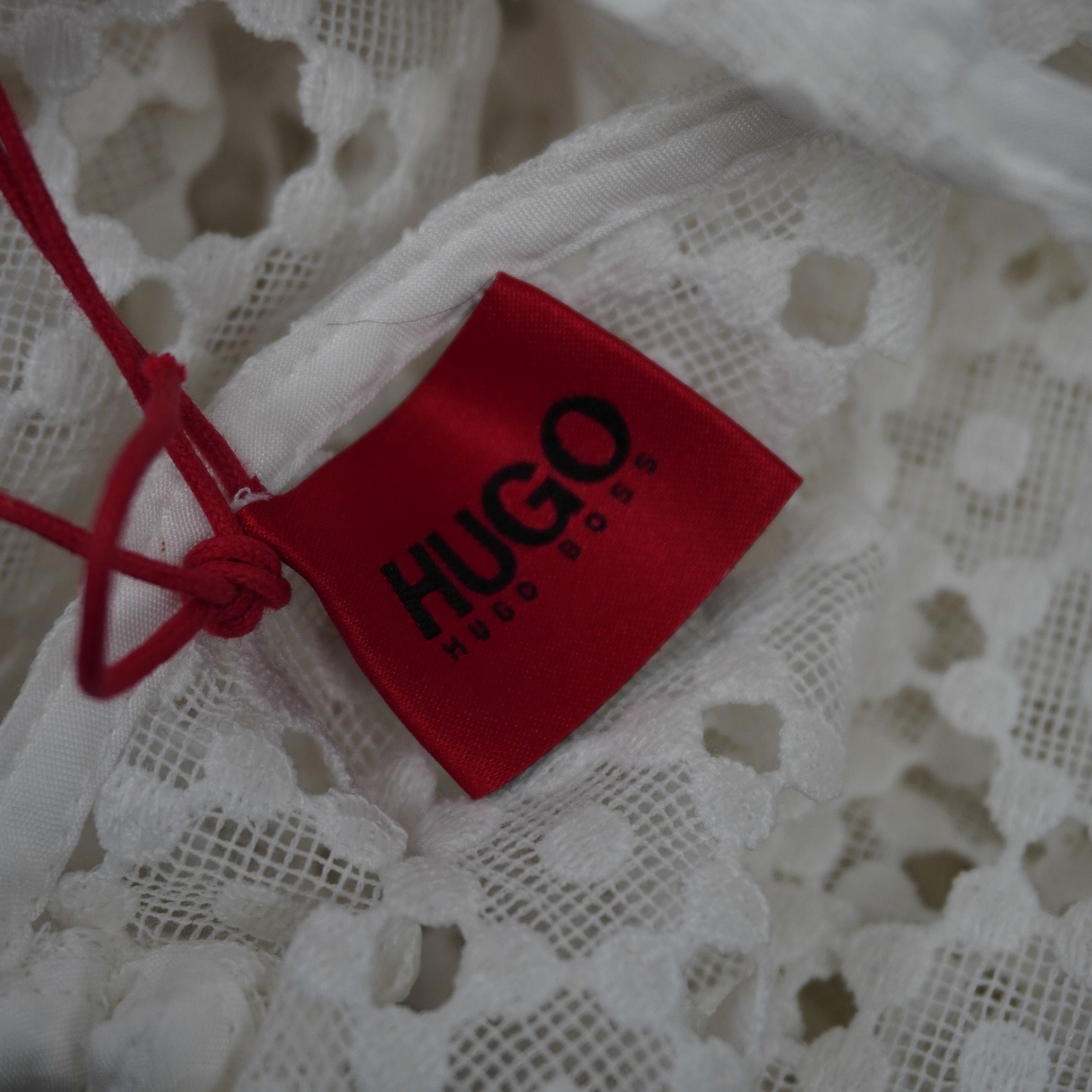 Cartellino rosso originale del brand HUGO Hugo Boss attaccato al tessuto traforato dell'abito bianco.