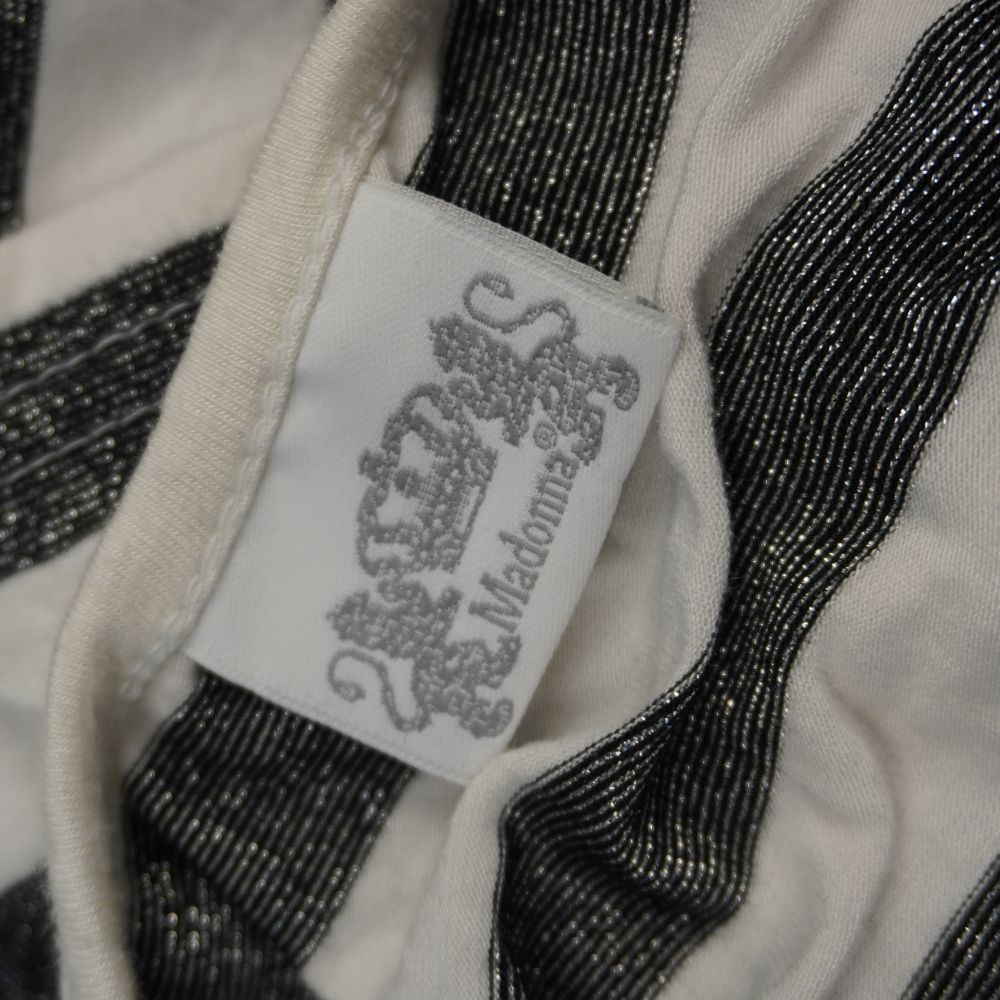 Dettaglio dell'etichetta interna in tessuto bianco del brand originale di Madonna con logo raffigurante una corona araldica e due leoni.